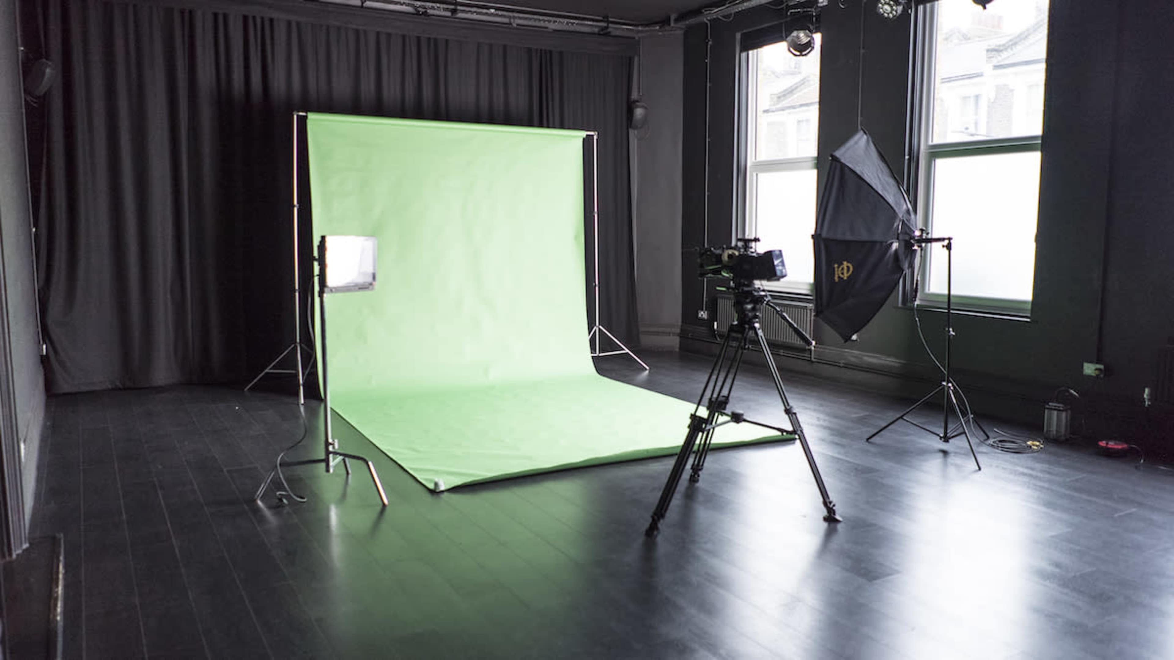 The image shows a photography studio featuring a green backdrop, studio lights, and a camera setup on a tripod.