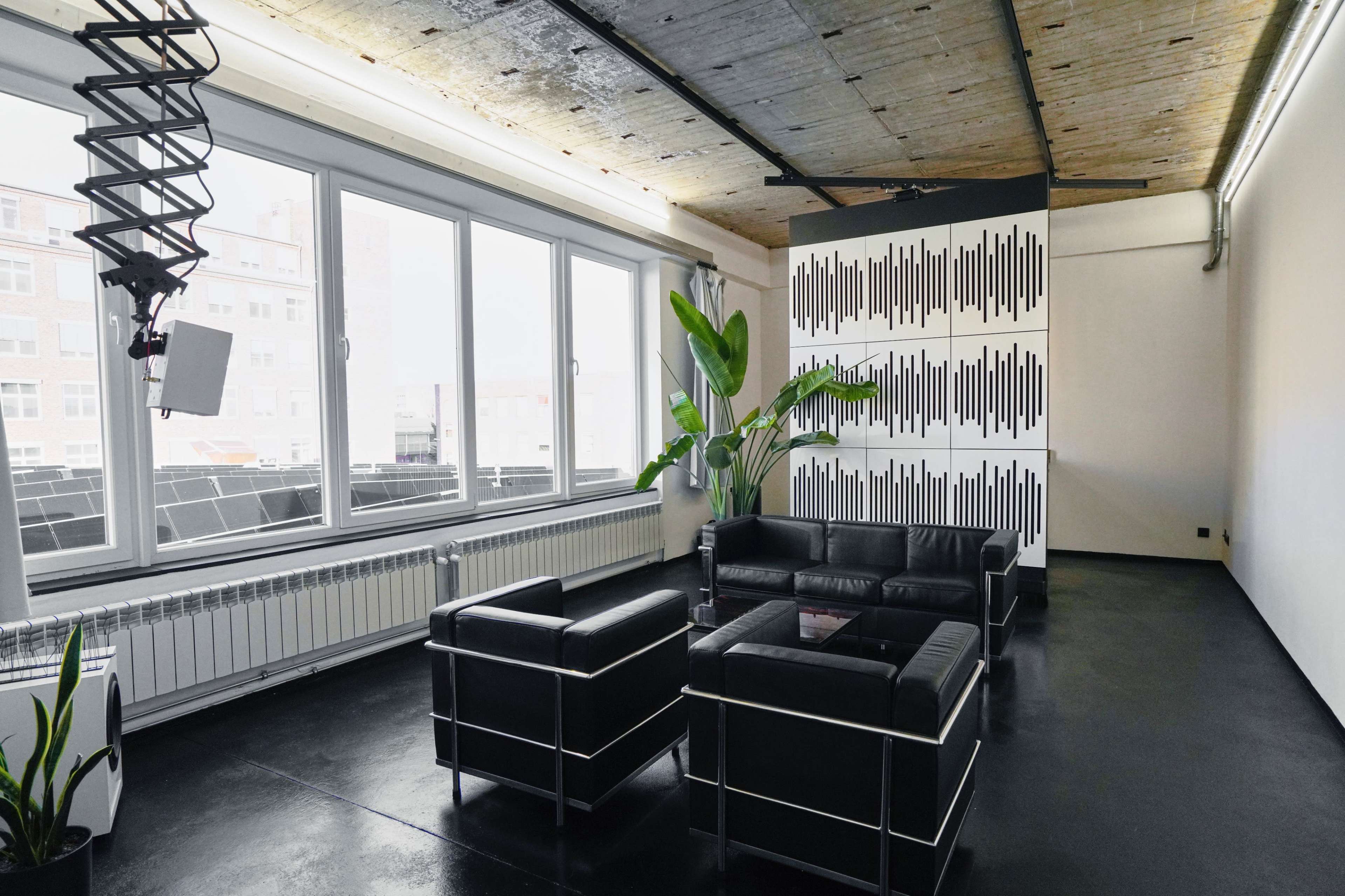 A spacious room with large windows, featuring black leather furniture and a patterned wall design.
