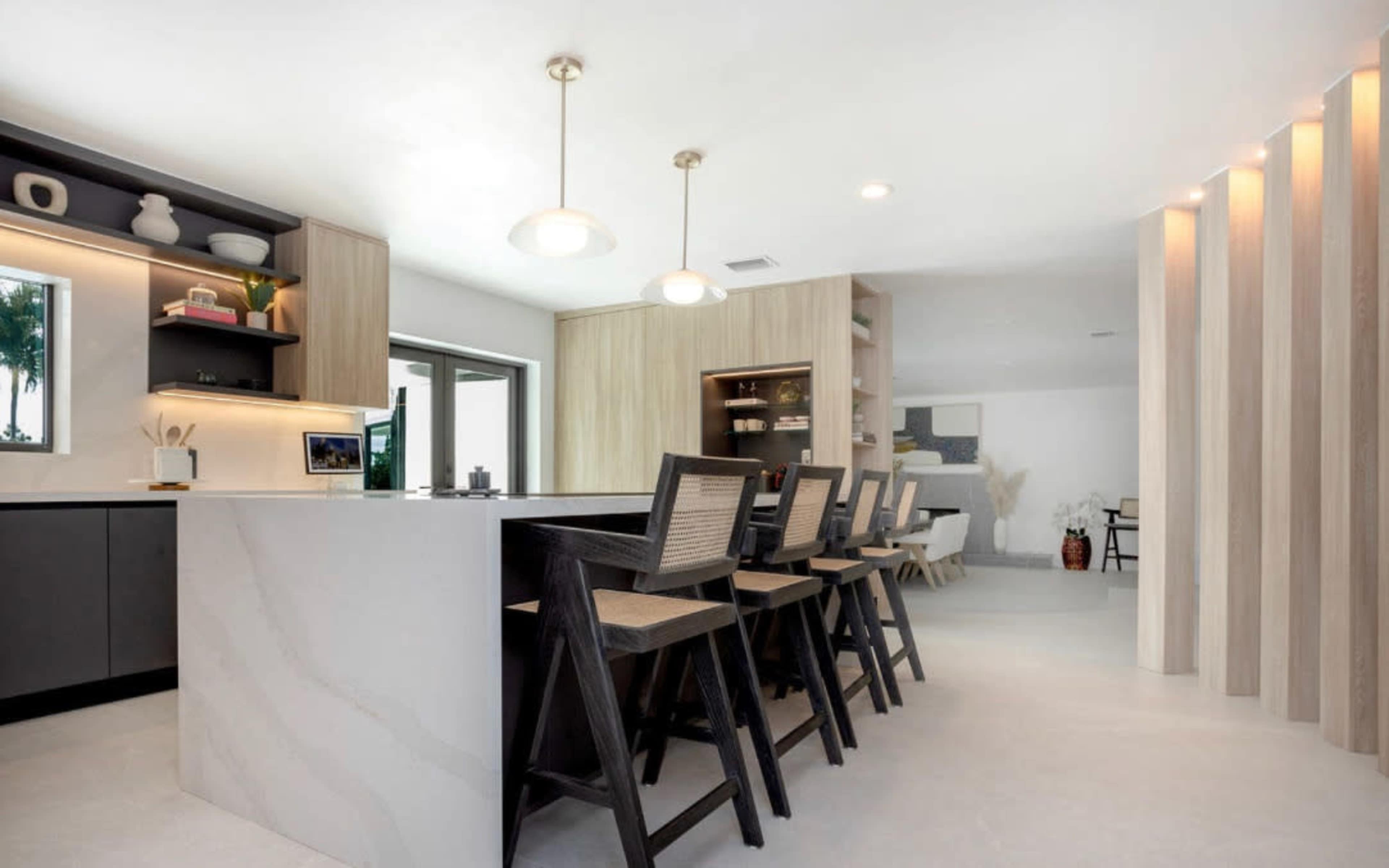 A modern kitchen with an island featuring bar seating, light wood cabinetry, and a clean, minimalist design.