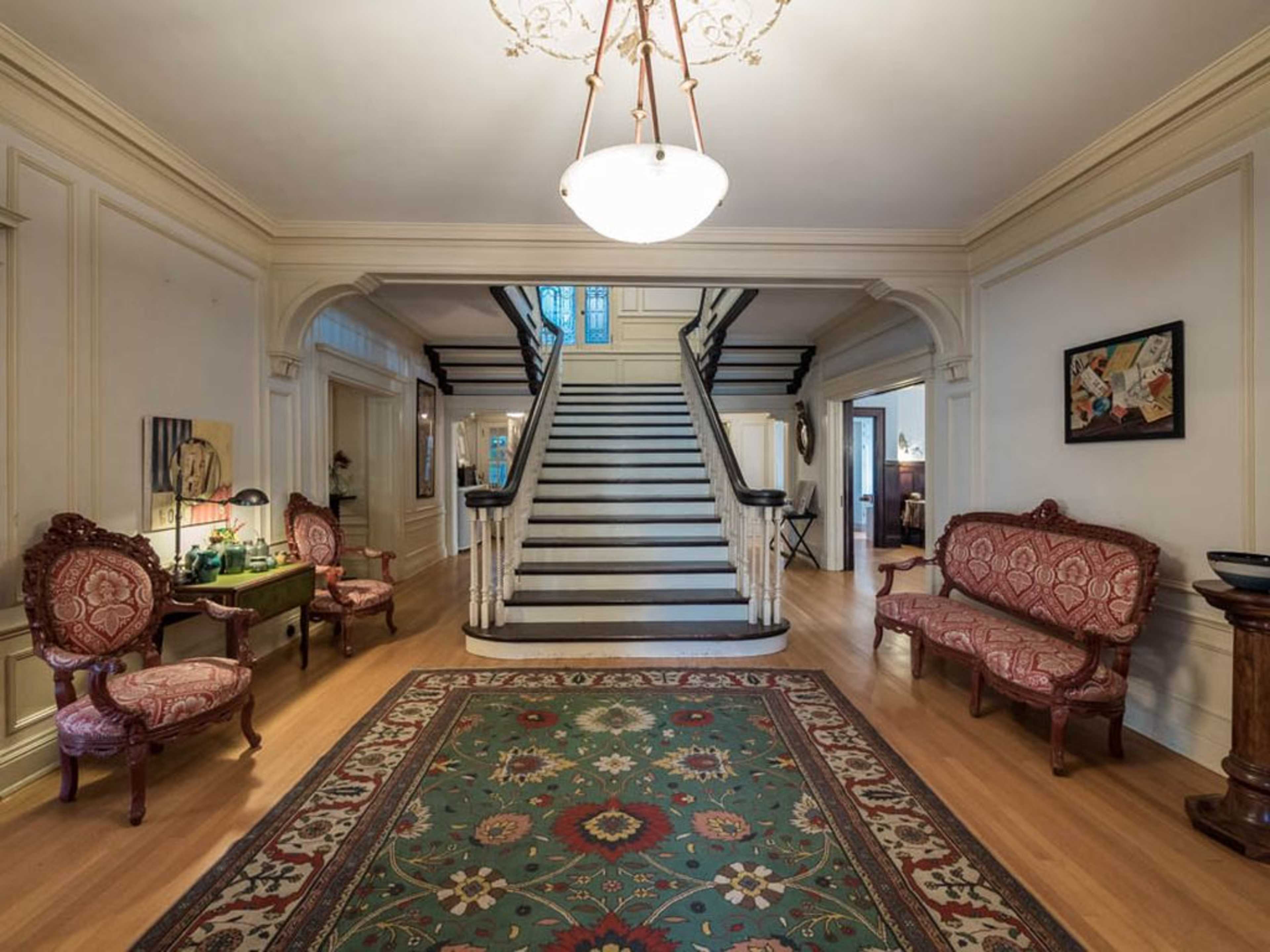A large foyer featuring a staircase, two ornate chairs, and a decorative rug on a wooden floor.