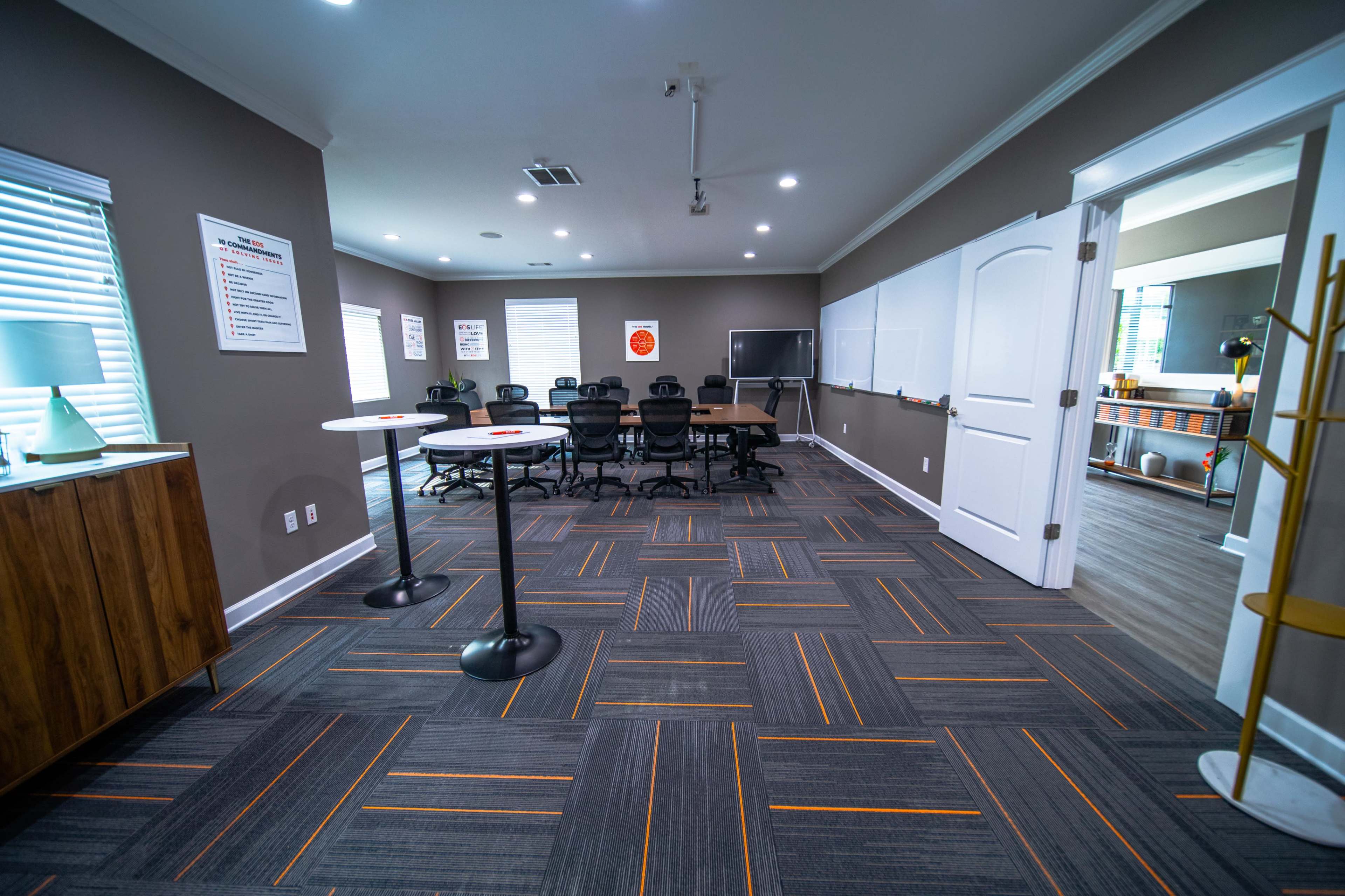 A modern conference room featuring a large table, several chairs, and whiteboards against a gray wall.