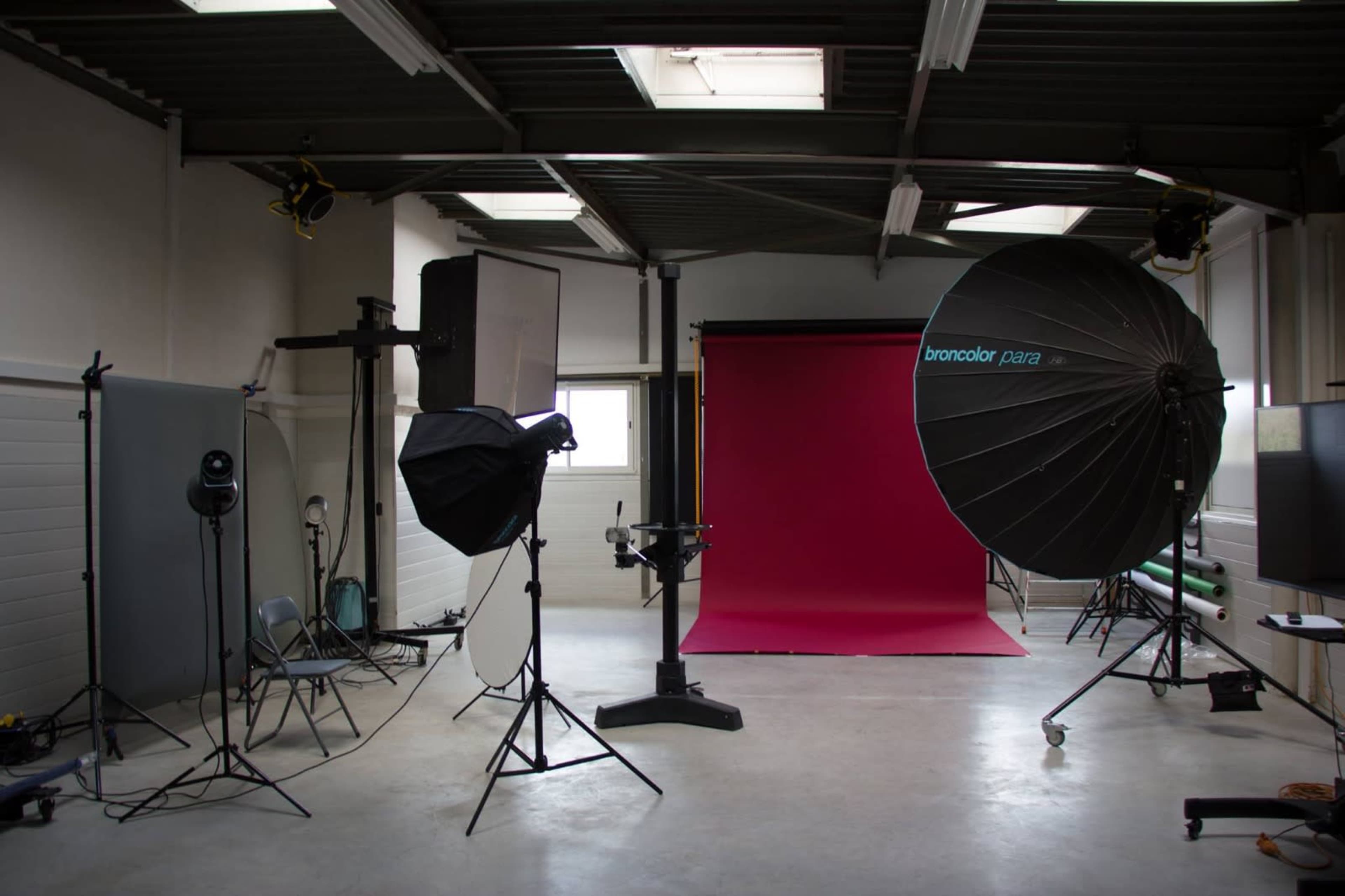 A photography studio is set up with various lighting equipment and a pink backdrop.