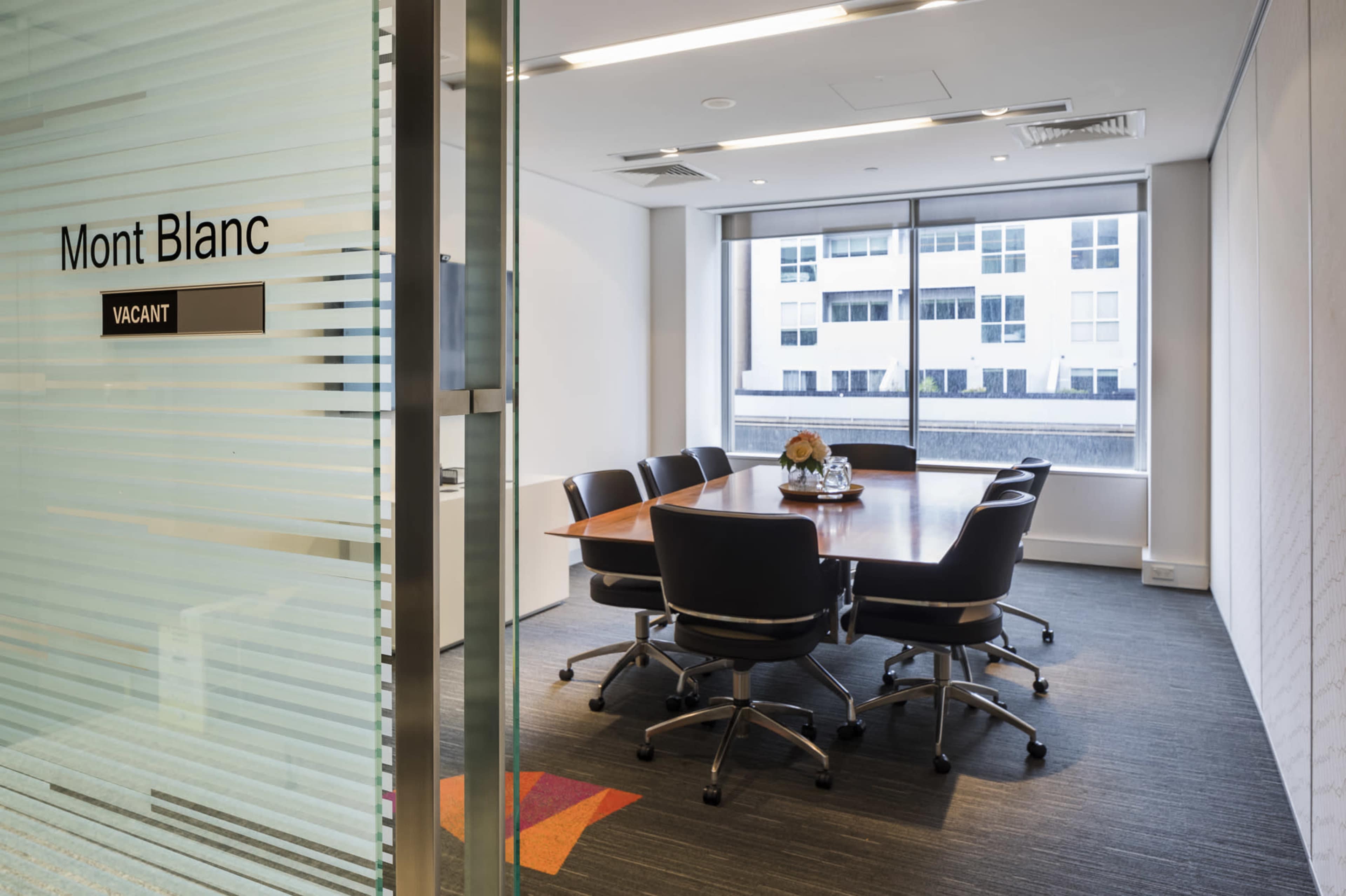 A conference room with a large wooden table and several black chairs is visible through a glass door labeled "Mont Blanc" and marked as "VACANT."