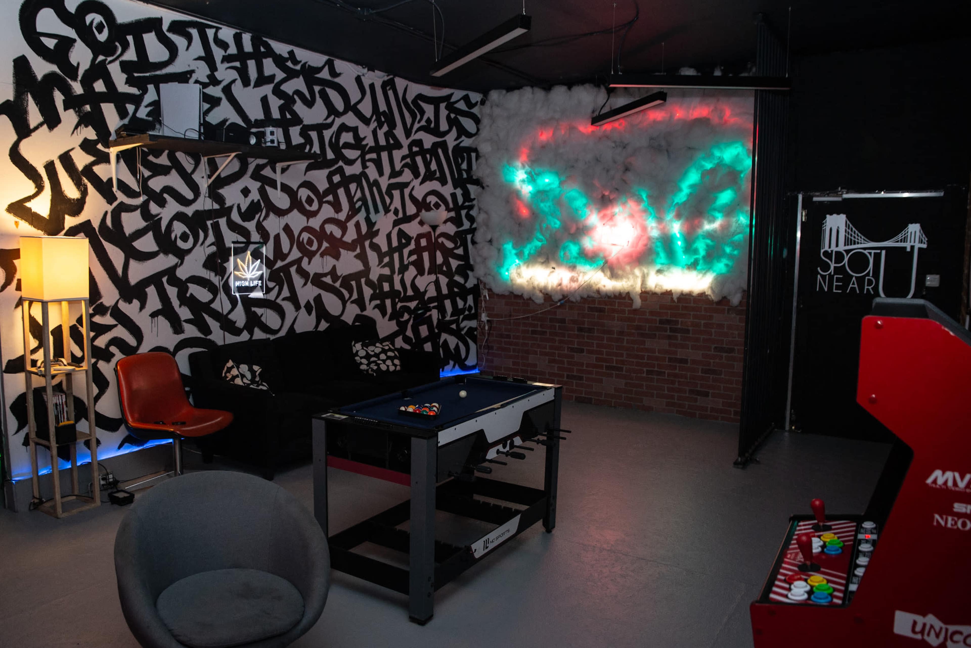 The image shows a recreational room with a pool table, colorful wall art, and a retro arcade machine.