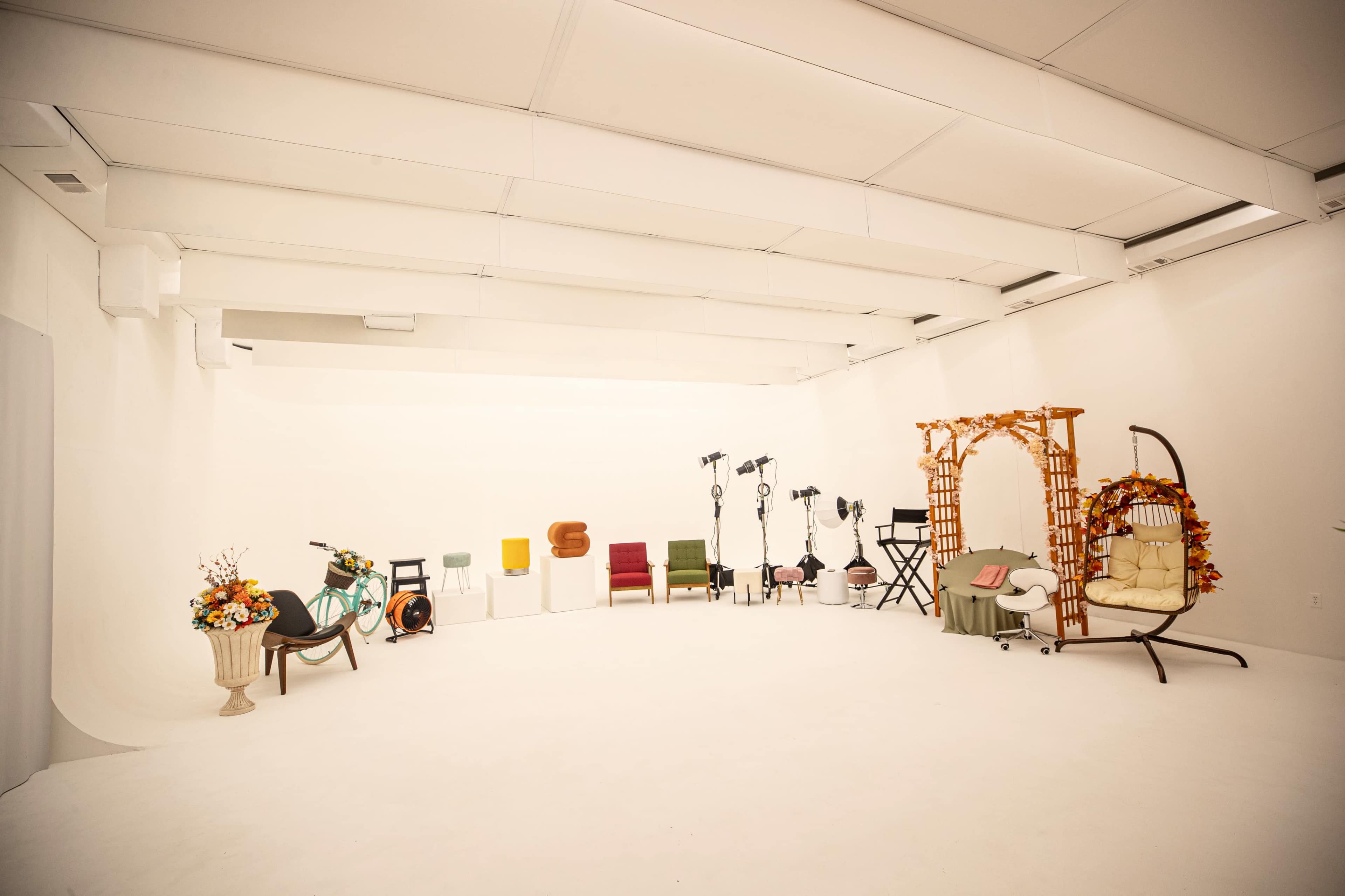 The image shows a spacious studio with various chairs, props, and lighting equipment arranged against a plain white backdrop.