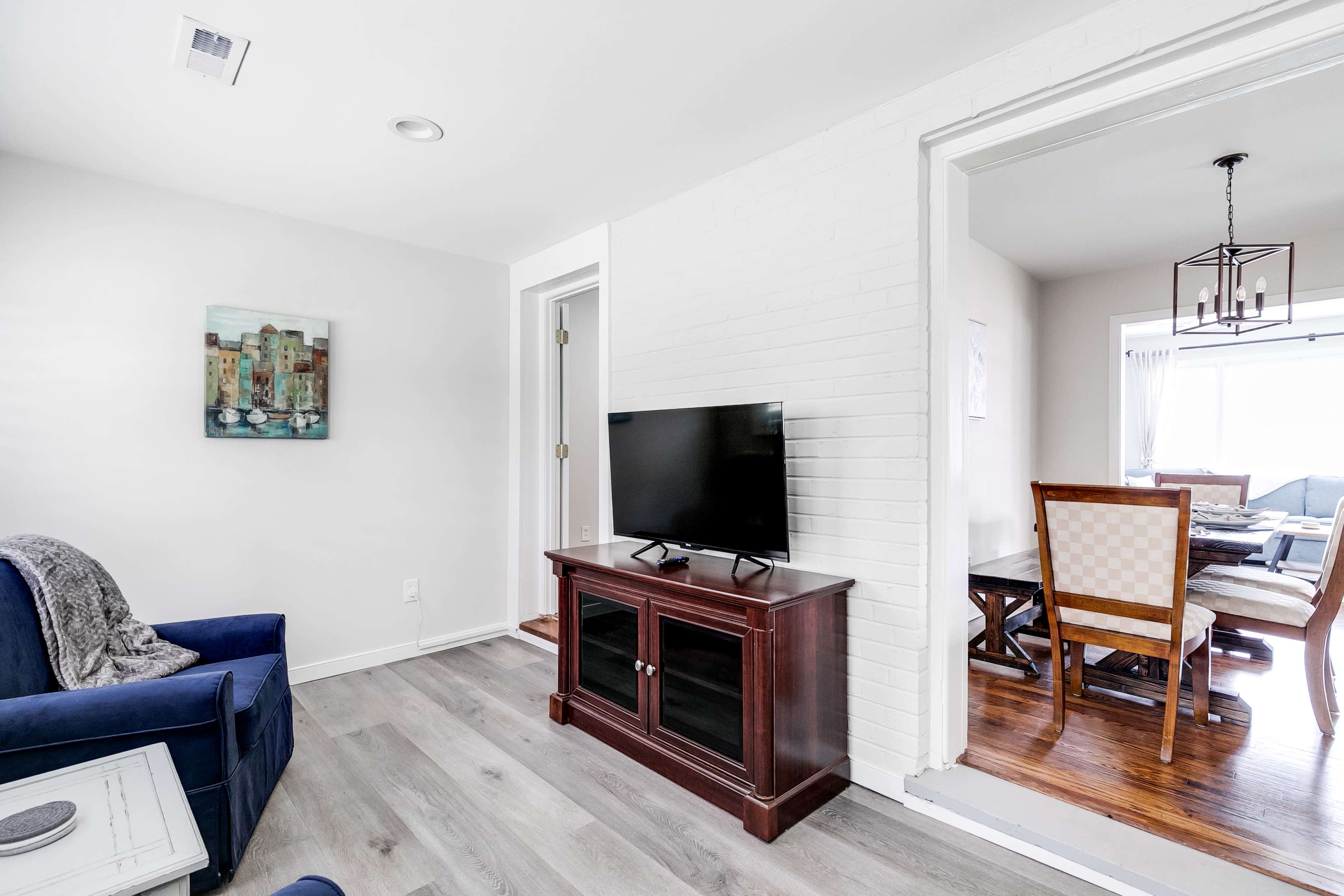 A living room features a television on a wooden cabinet, a blue couch, and a doorway leading to a dining area.