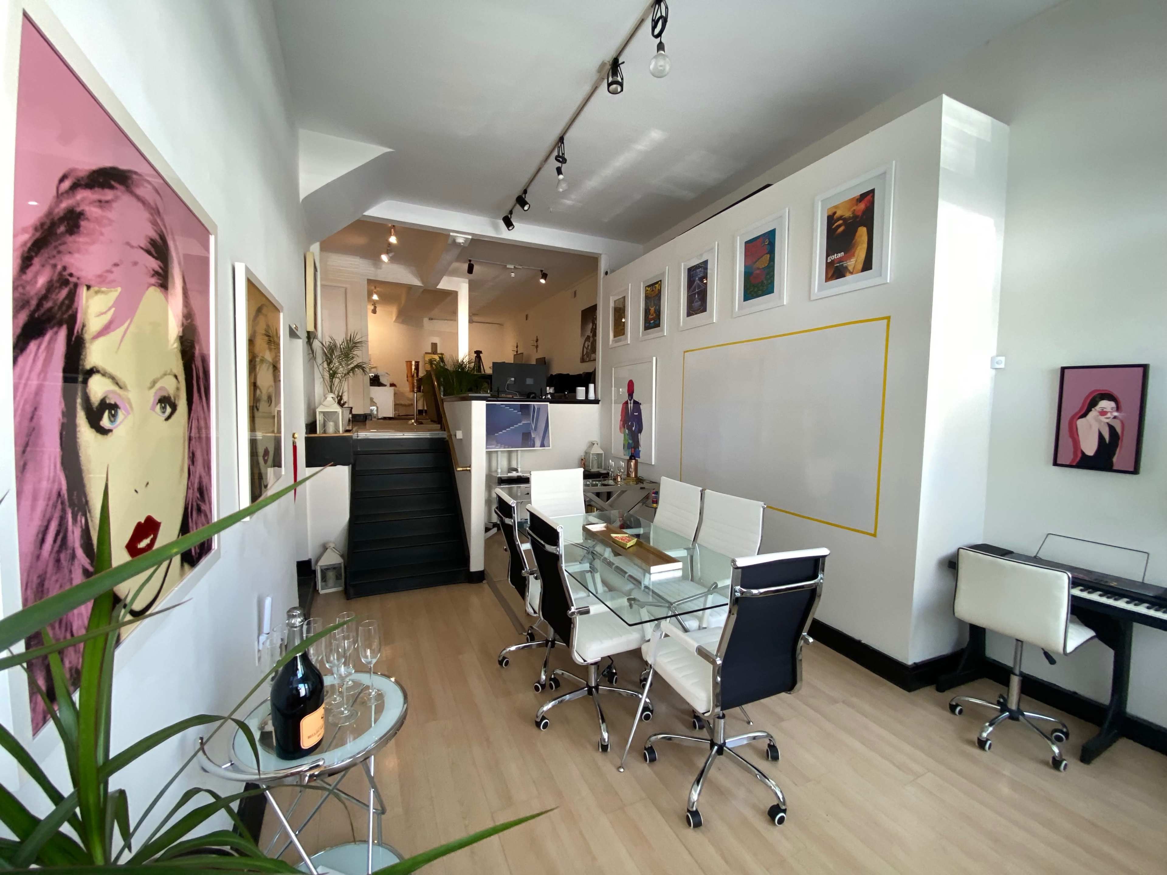 The image shows a modern office space with a glass conference table, white chairs, and various framed artworks on the walls.