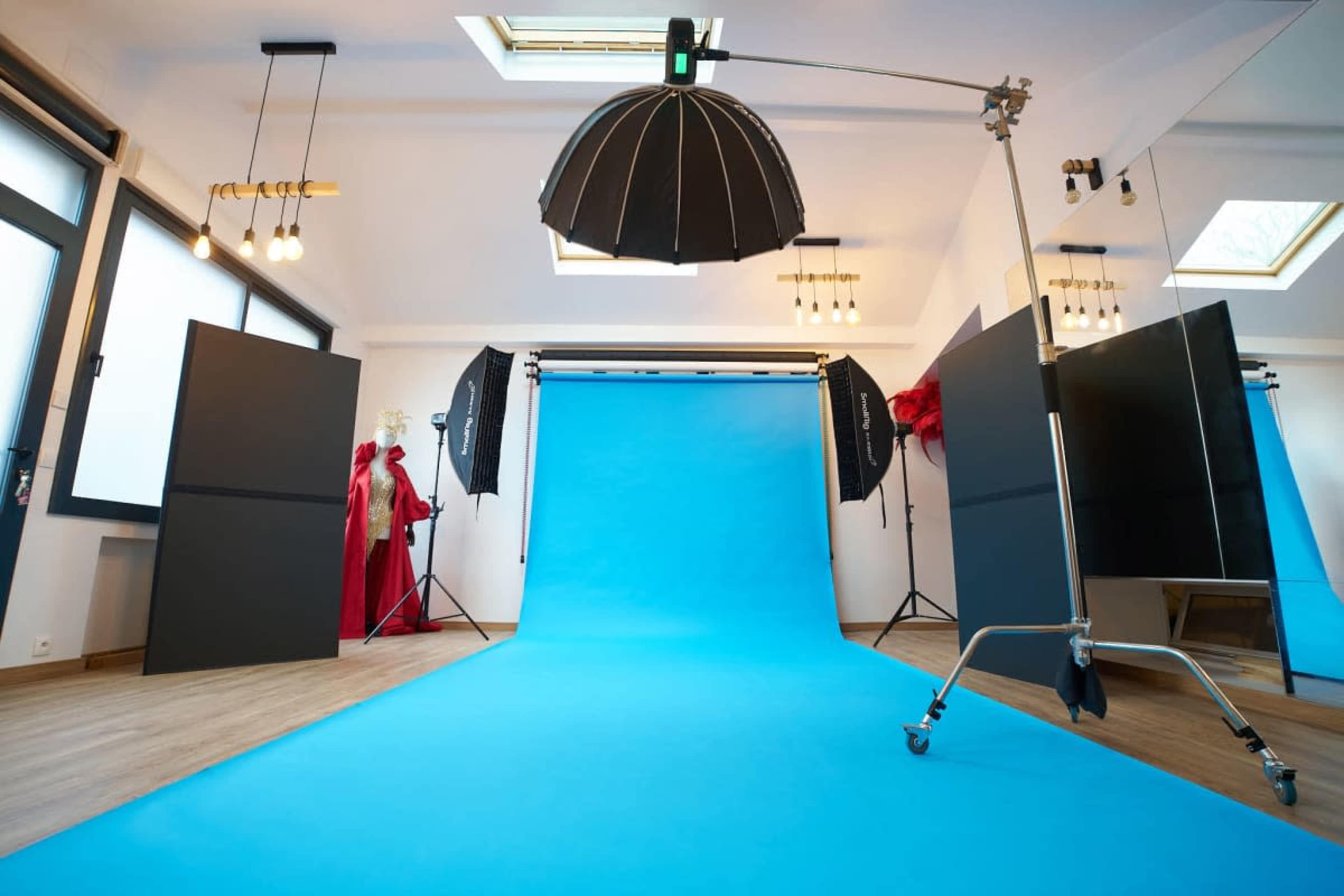 The image shows a photography studio with a bright blue backdrop, lighting equipment, and large black panels arranged around the space.