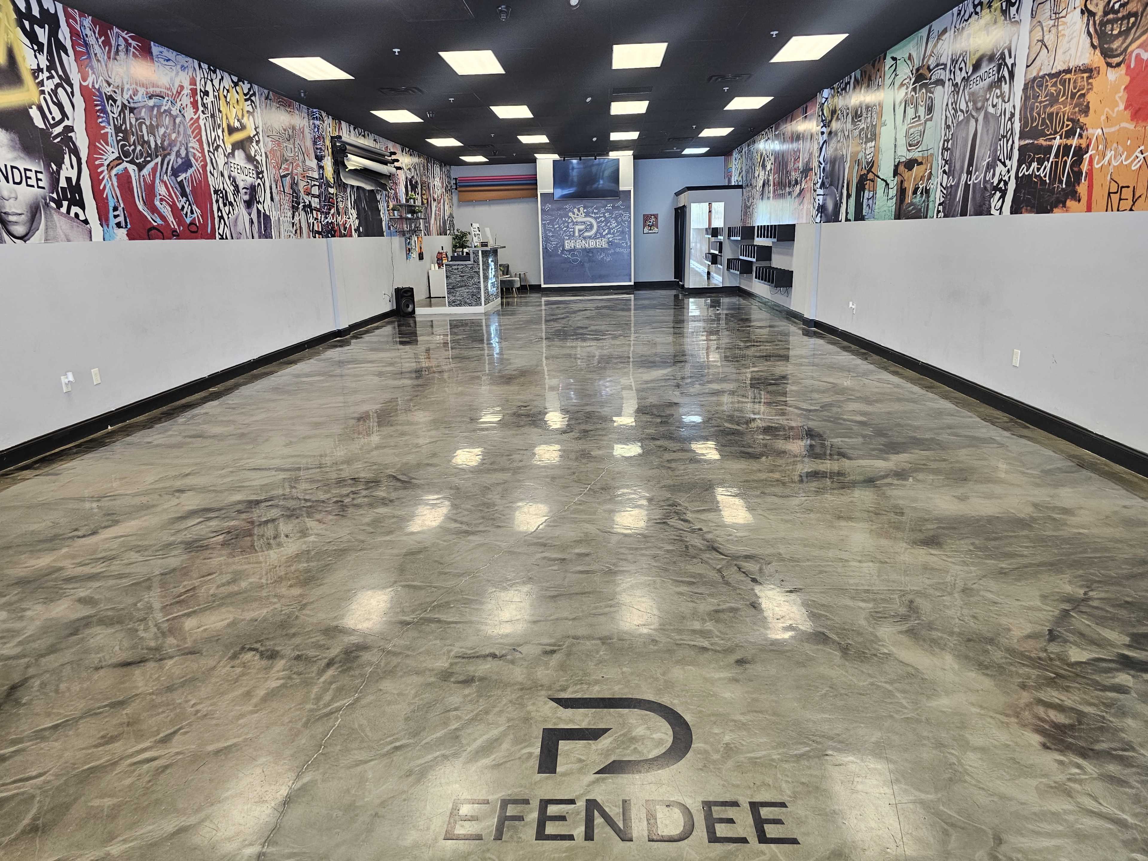 The image shows a spacious indoor area with polished concrete floors, colorful graffiti art on the walls, and a reception desk at the far end.