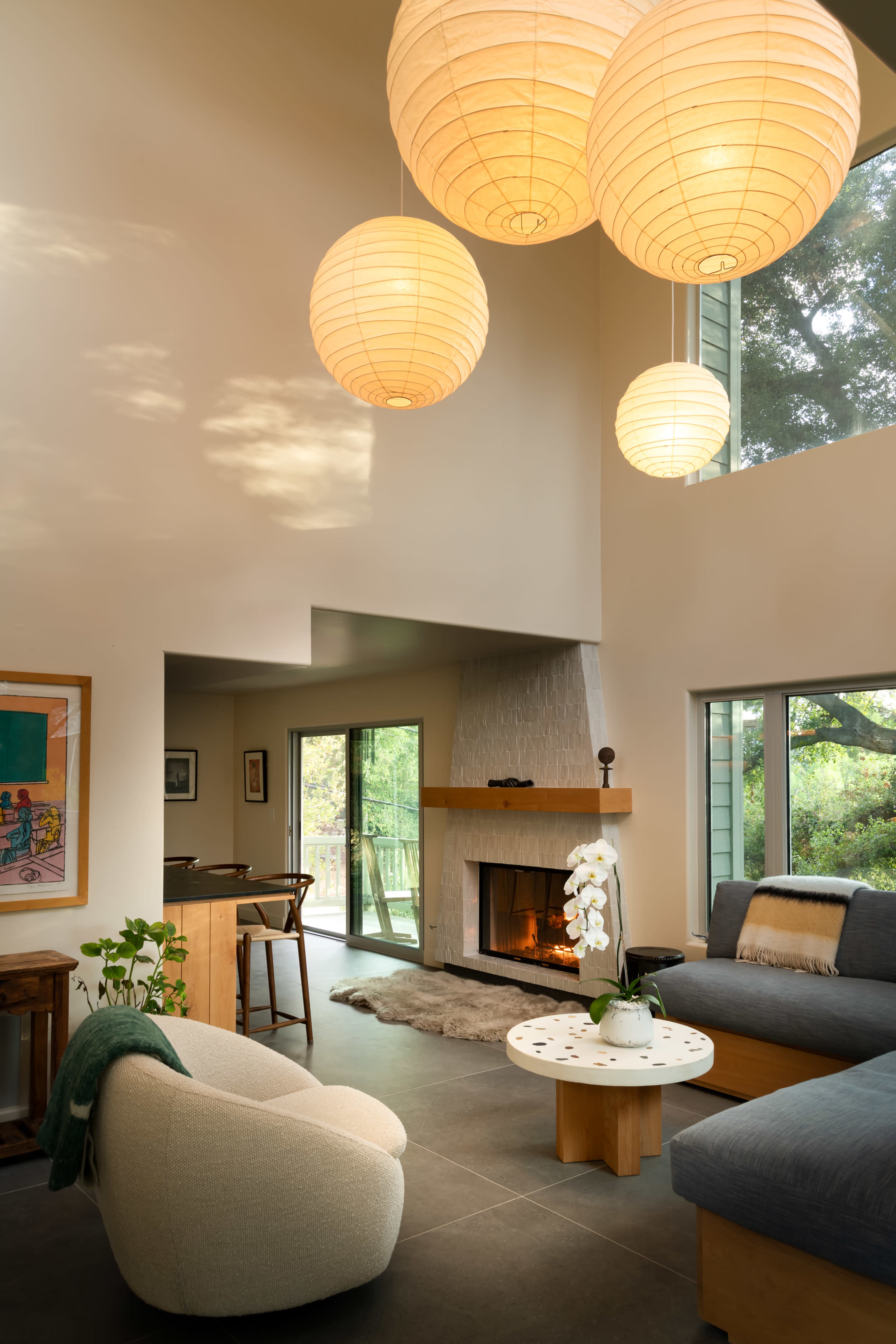 The image shows a modern living room with large windows, a cozy fireplace, a sofa, and decorative pendant lights.