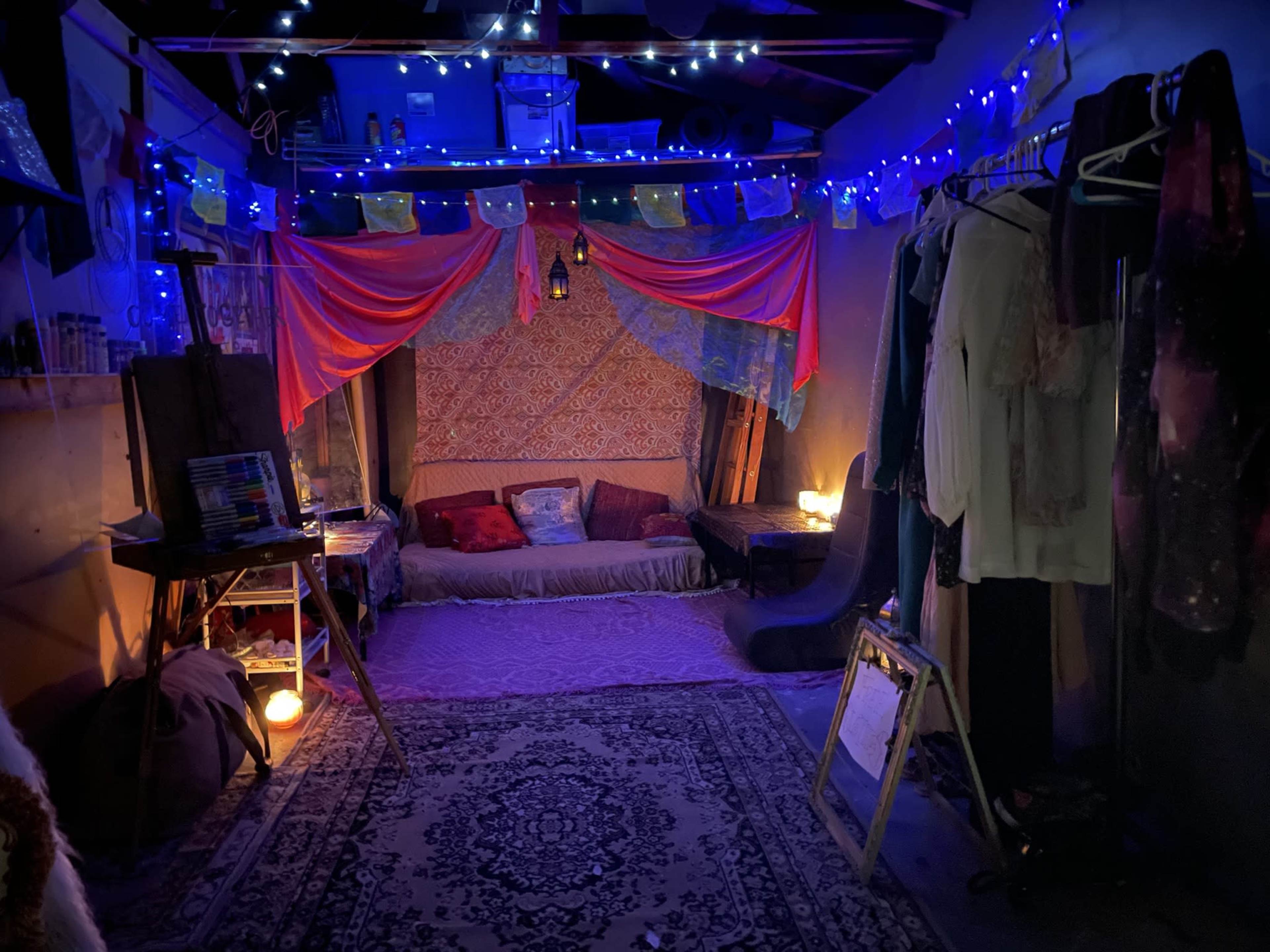 A cozy gathering space with colorful drapes, soft seating, and ambient lighting created by candles and string lights.