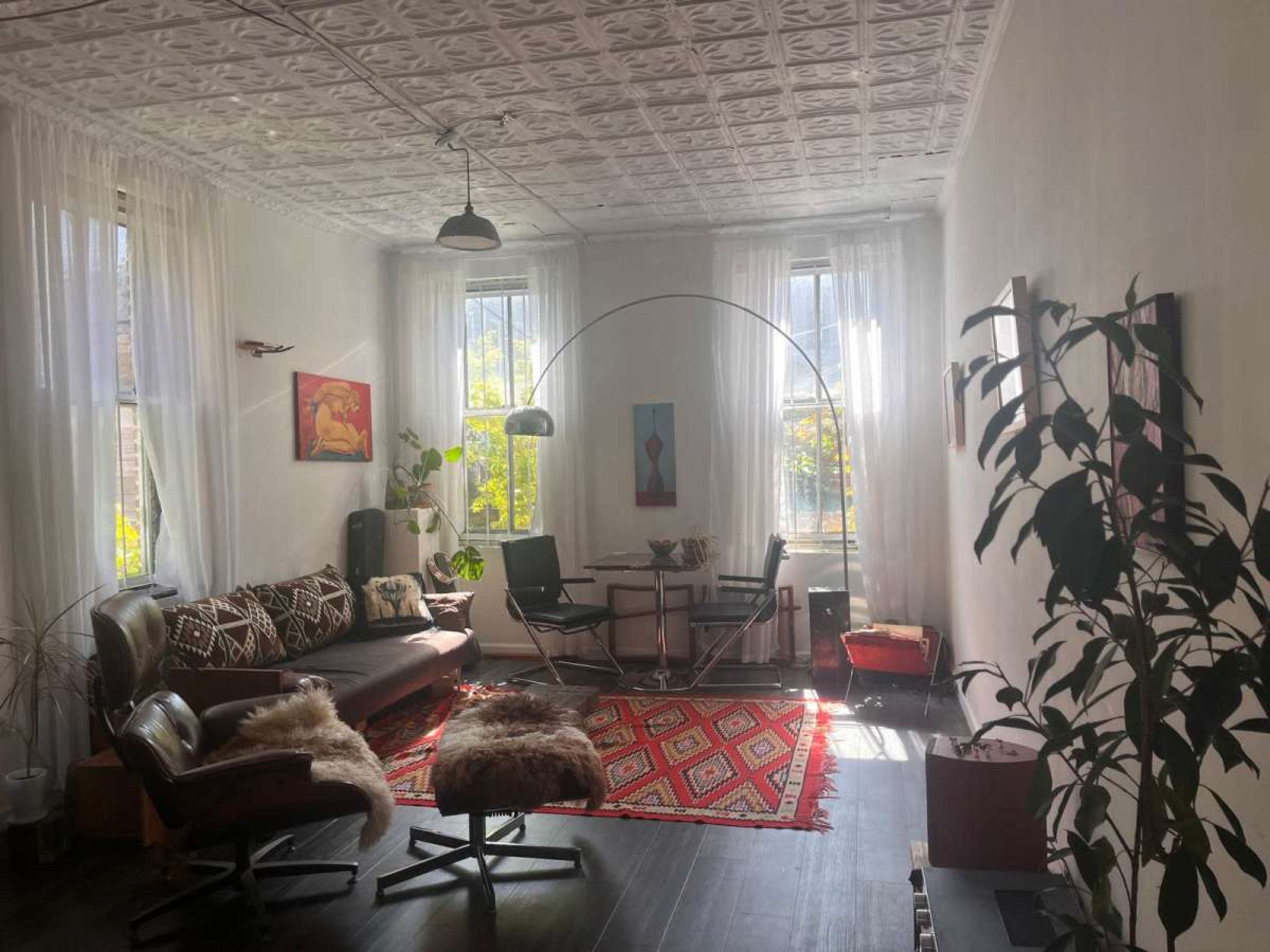 The image depicts a bright living room featuring a mix of modern and vintage furniture, with large windows allowing natural light to illuminate the space.