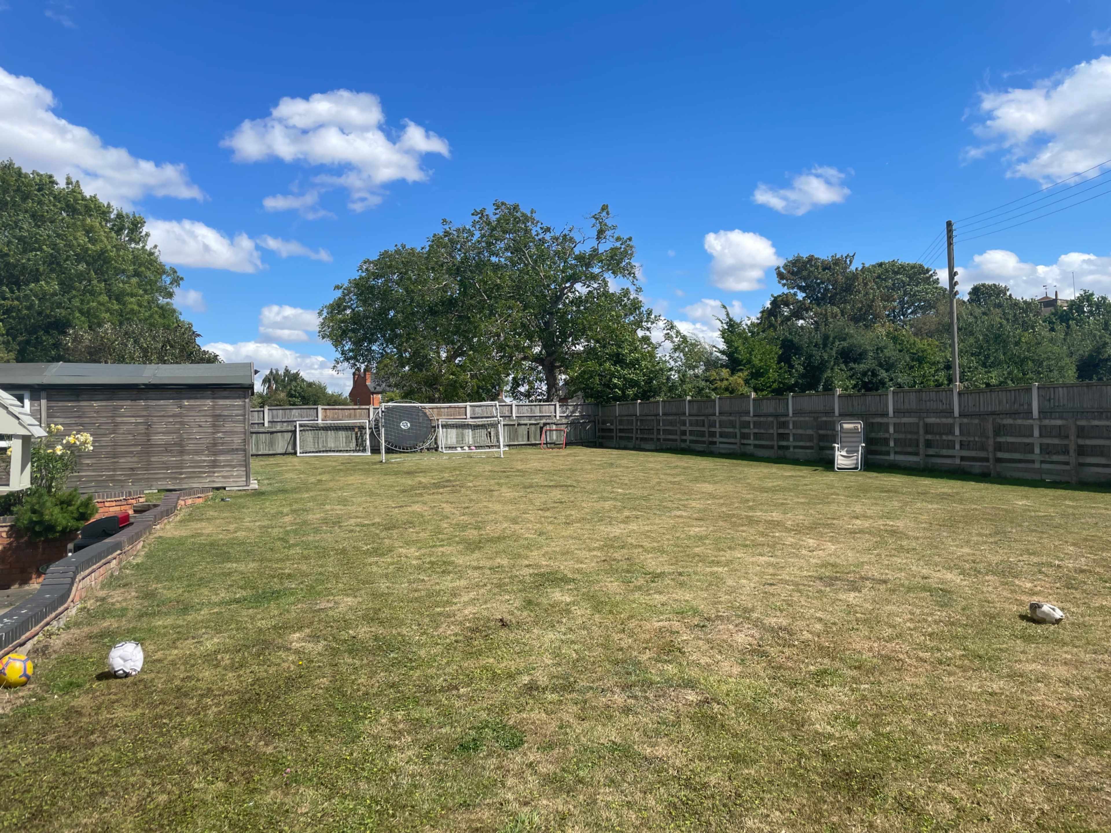 A large, open backyard with a grassy area, a fence surrounding it, and a few scattered objects.
