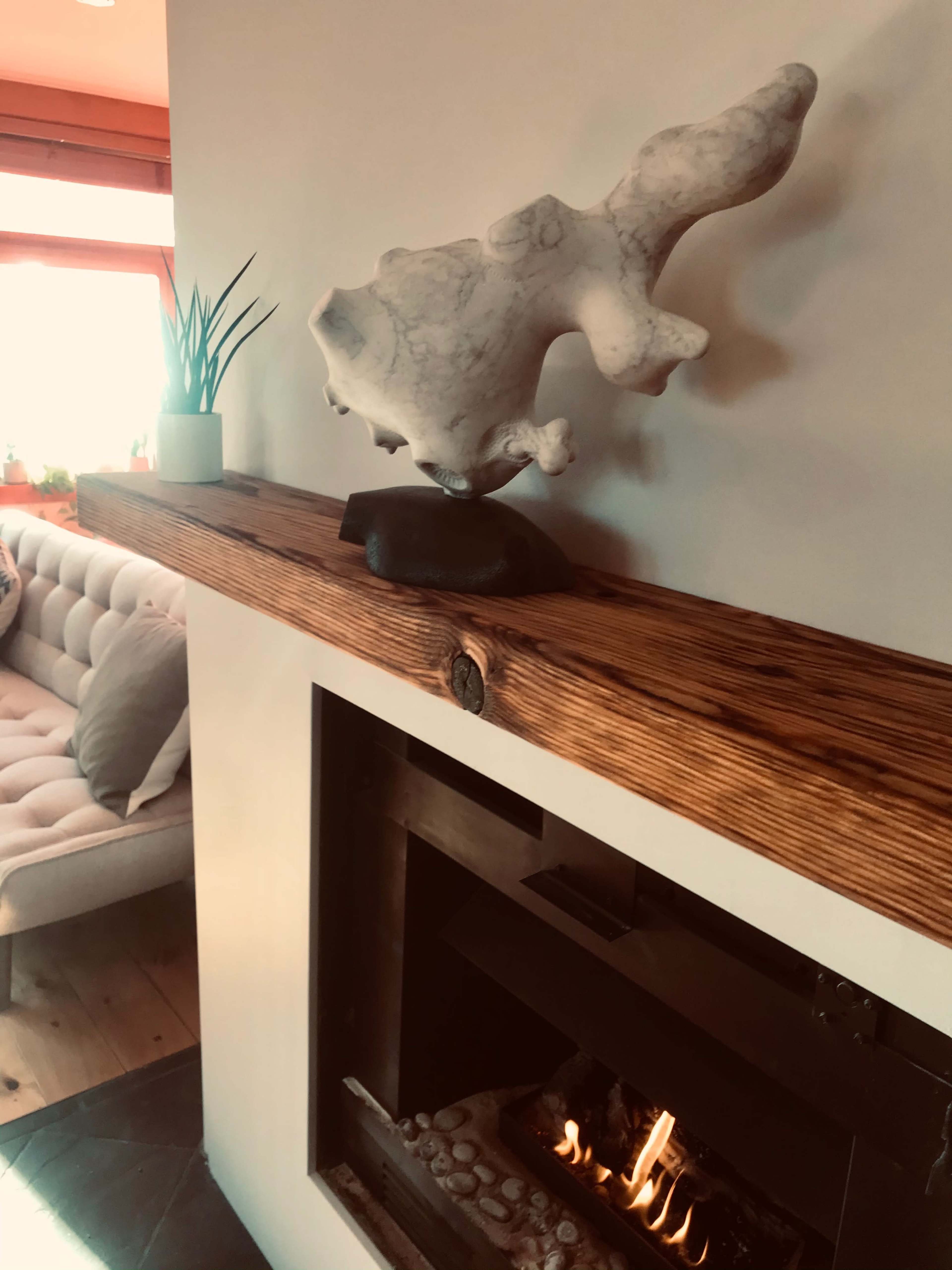 A marble sculpture is displayed on a wooden mantel above a modern fireplace with a small flame burning inside.