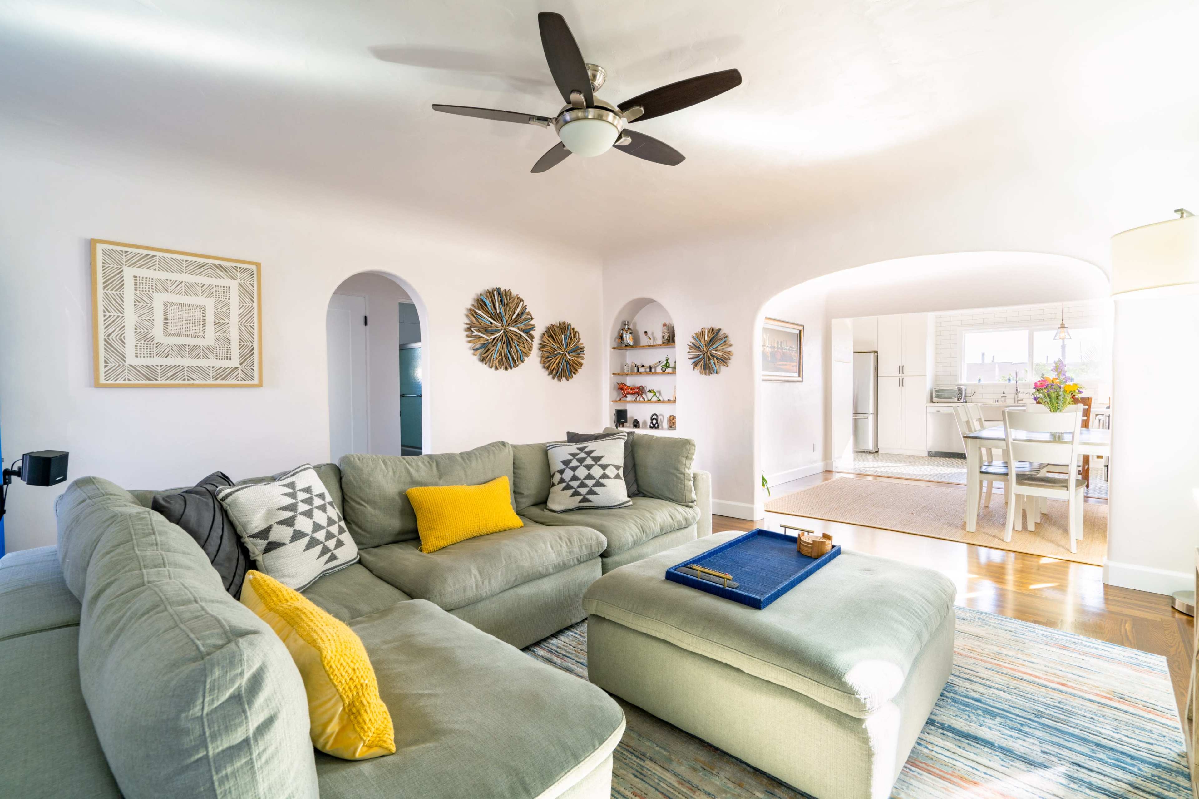 A spacious living room features a large, light green sectional sofa, a coffee table, and an open archway leading to a dining area.