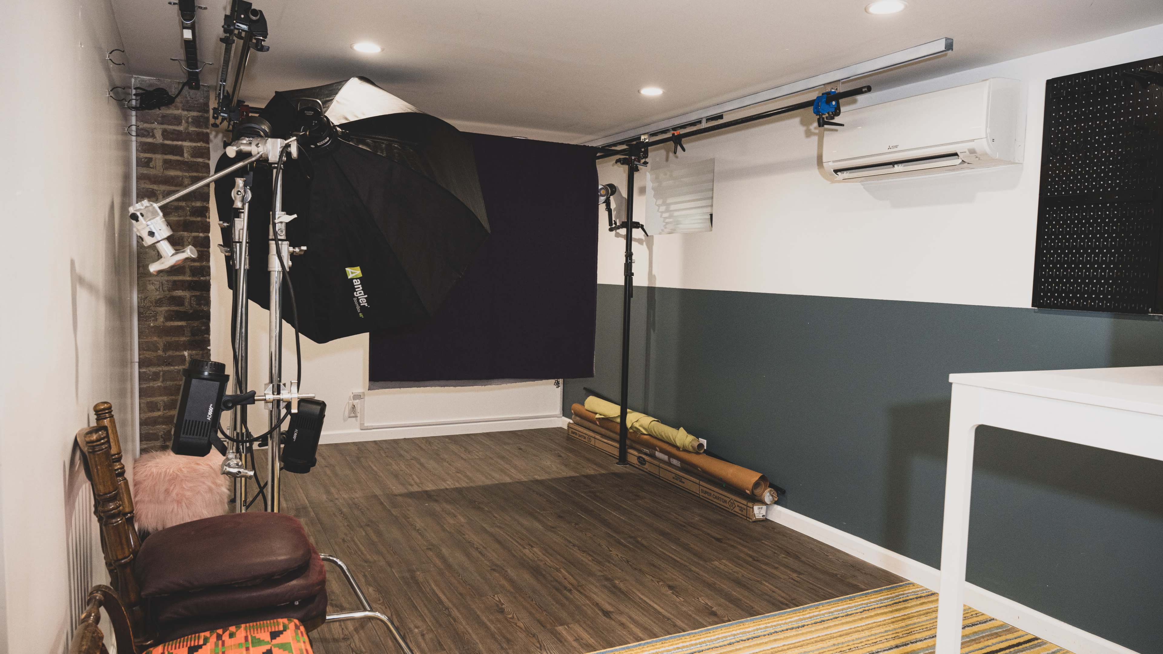 The image shows a photography studio with a lighting setup, backdrop, and various equipment arranged in a modern interior space.