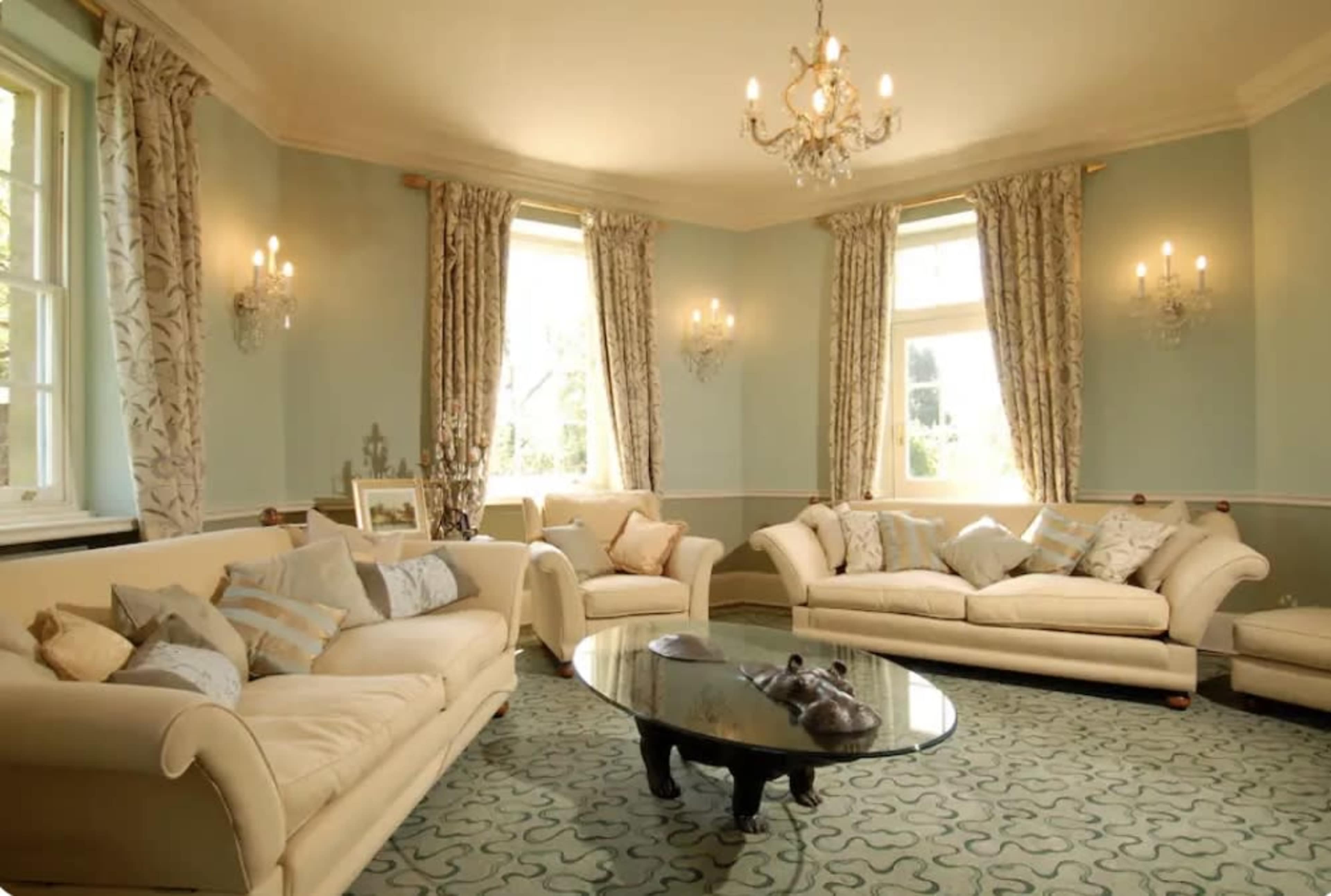 A spacious living room with two light-colored sofas, a dark coffee table, and large windows adorned with curtains.