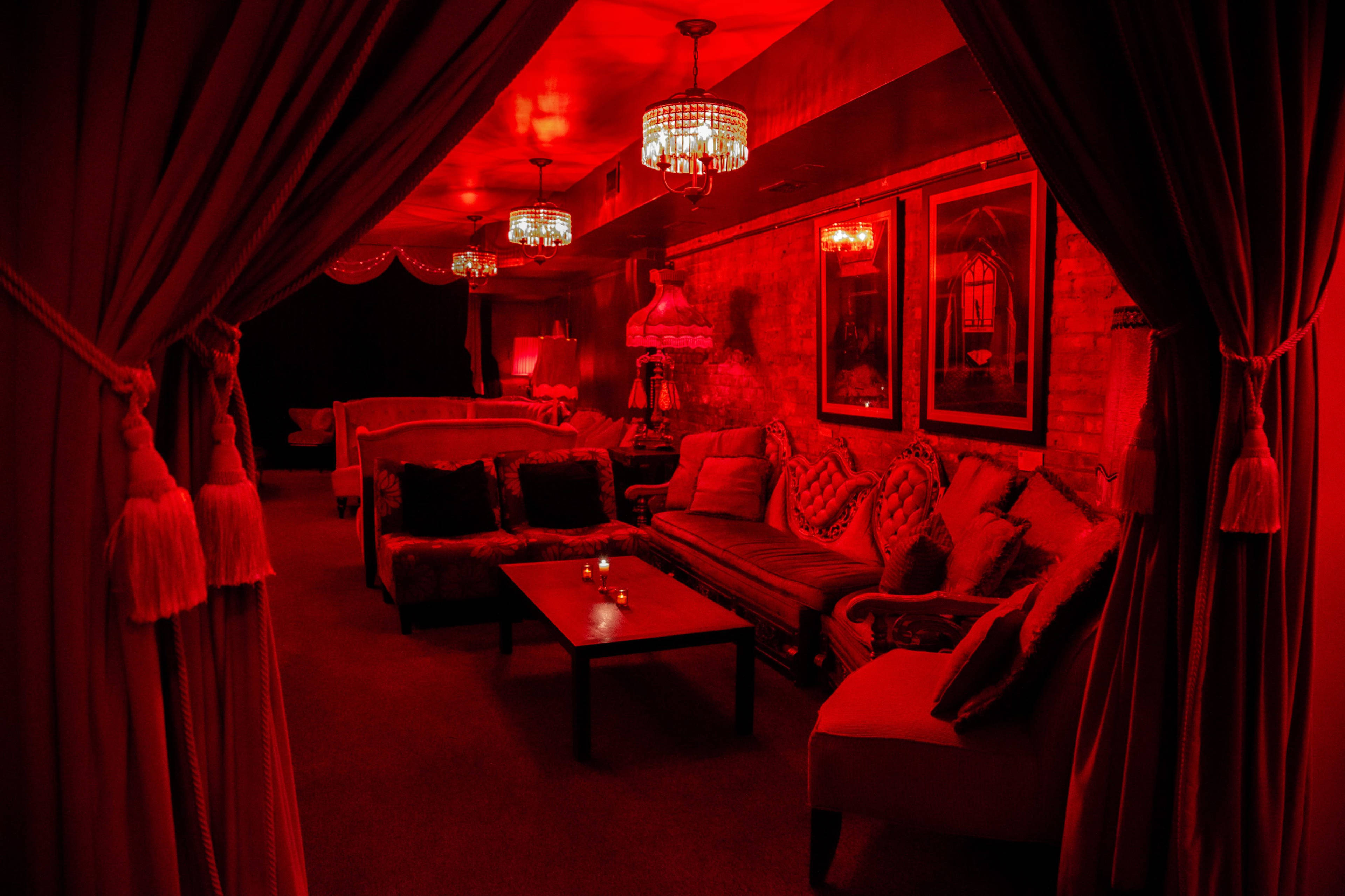 A lounge area is illuminated with red light, featuring plush seating and decorative chandeliers.