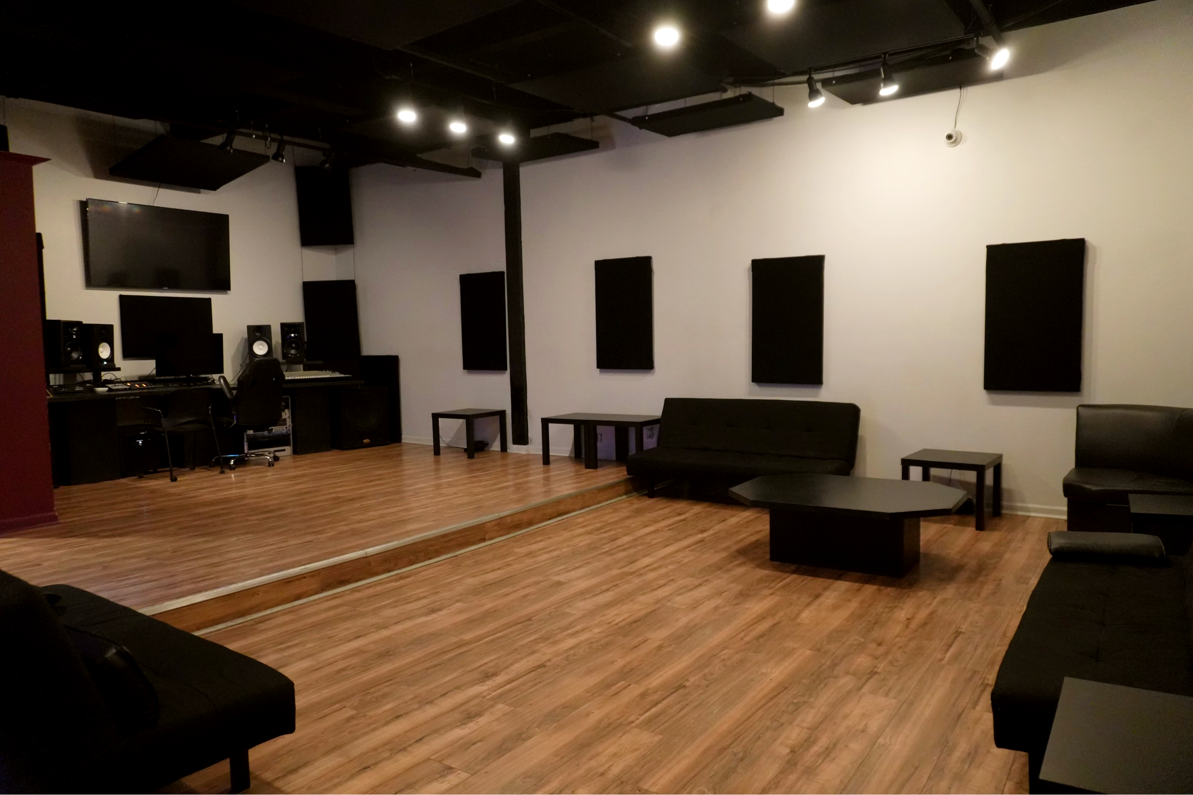 A music studio with soundproof panels on the walls, a mirrored area, and seating arranged around a low coffee table.