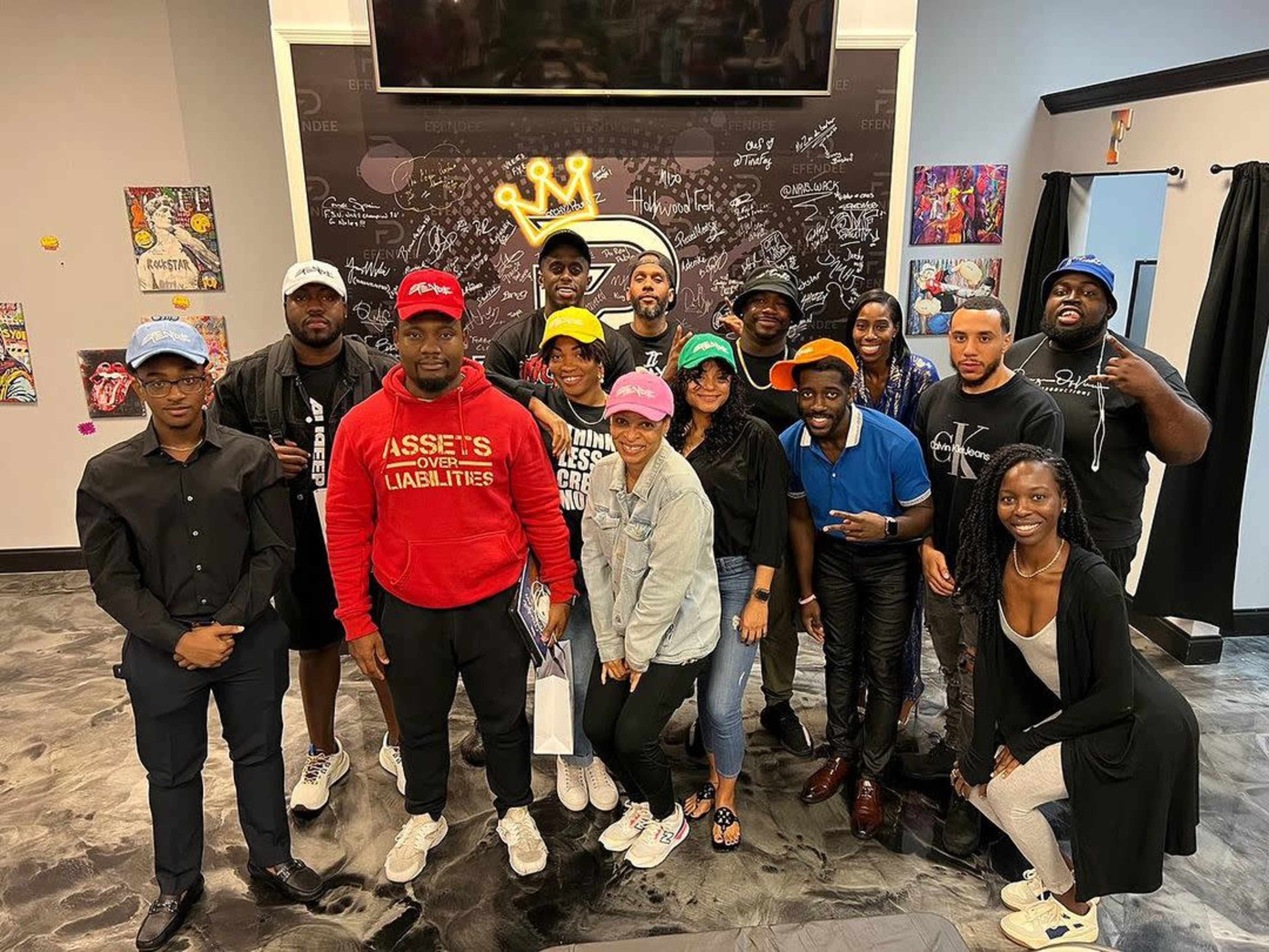 A group of people stands together in a room with a mural and various colorful hats.