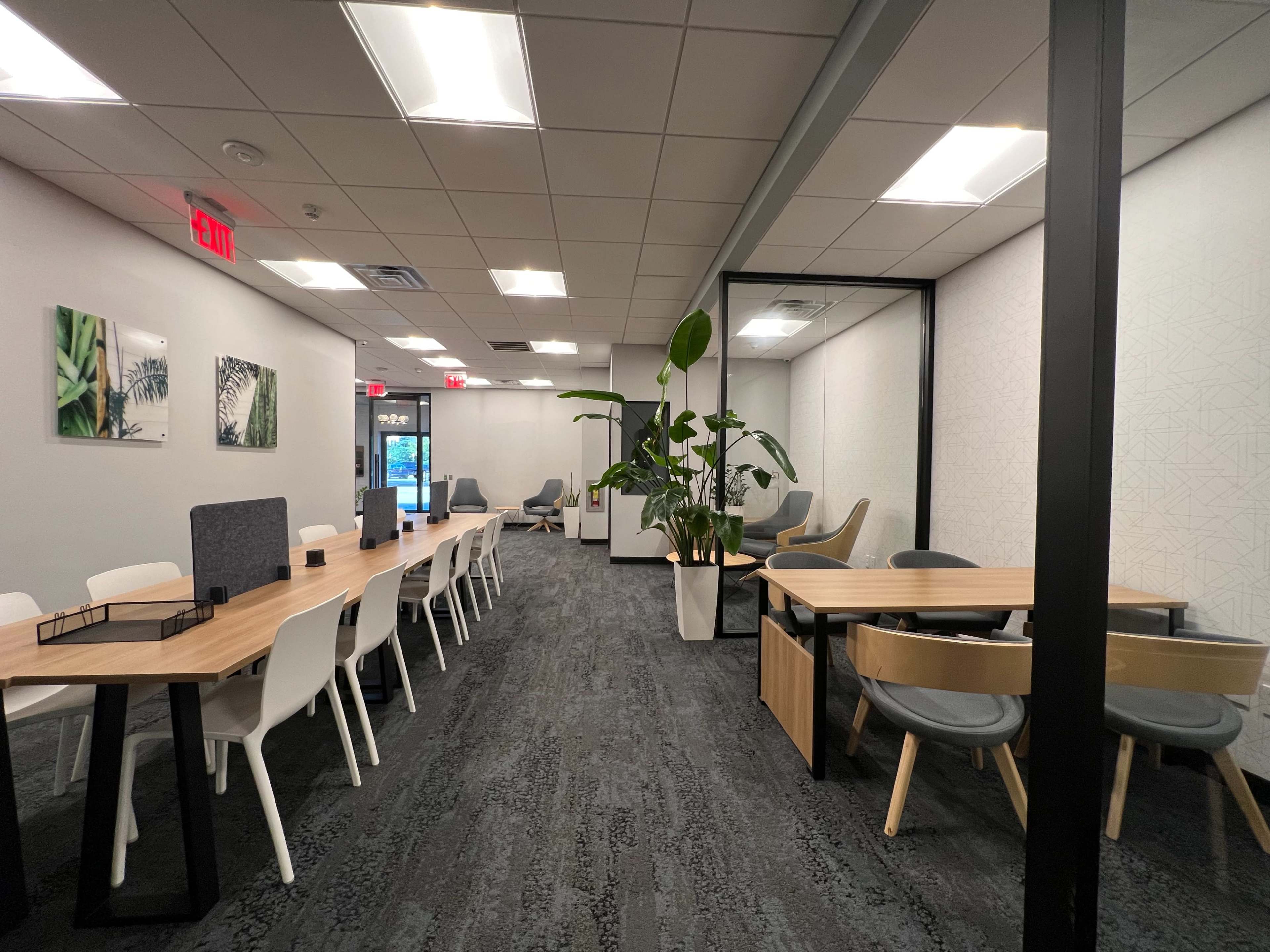 A modern office space with a long table, chairs, and a separate meeting area featuring plants and artwork on the walls.