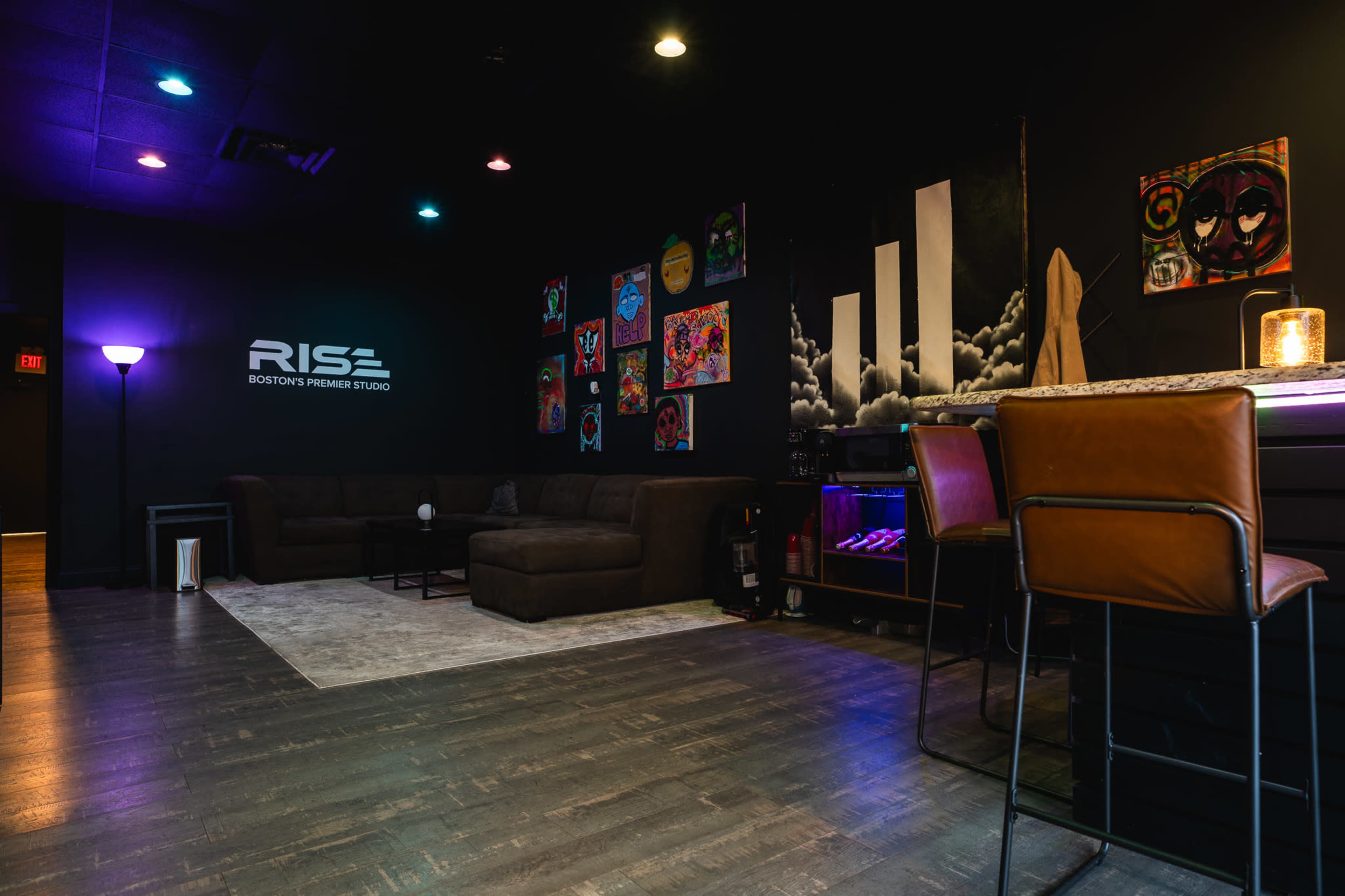 The image shows a stylish lounge area with a dark wall, artistic decorations, a large sectional sofa, and a bar with high stools.