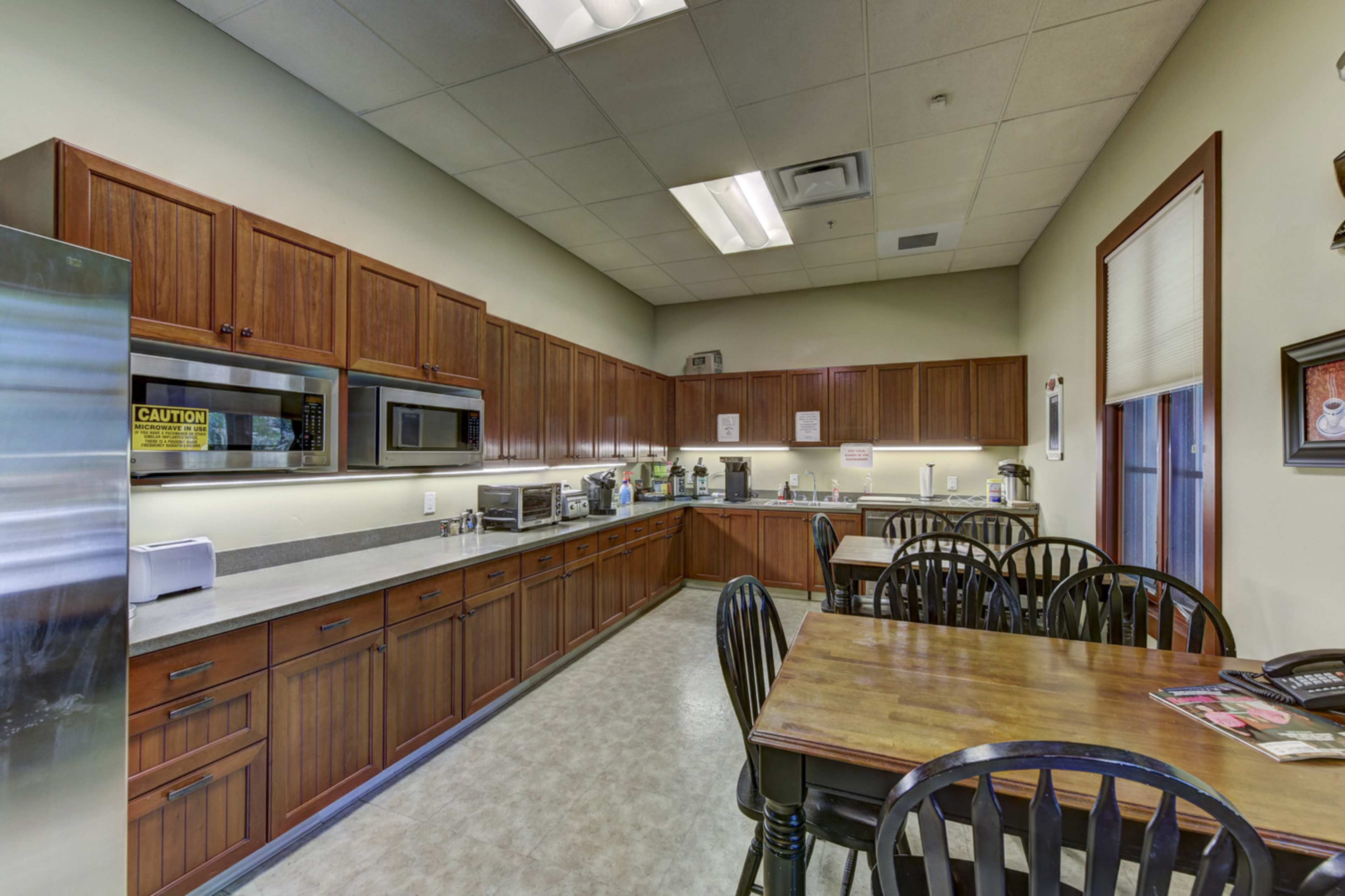 A kitchen with wooden cabinets, a countertop, various kitchen appliances, and a dining table with black chairs.