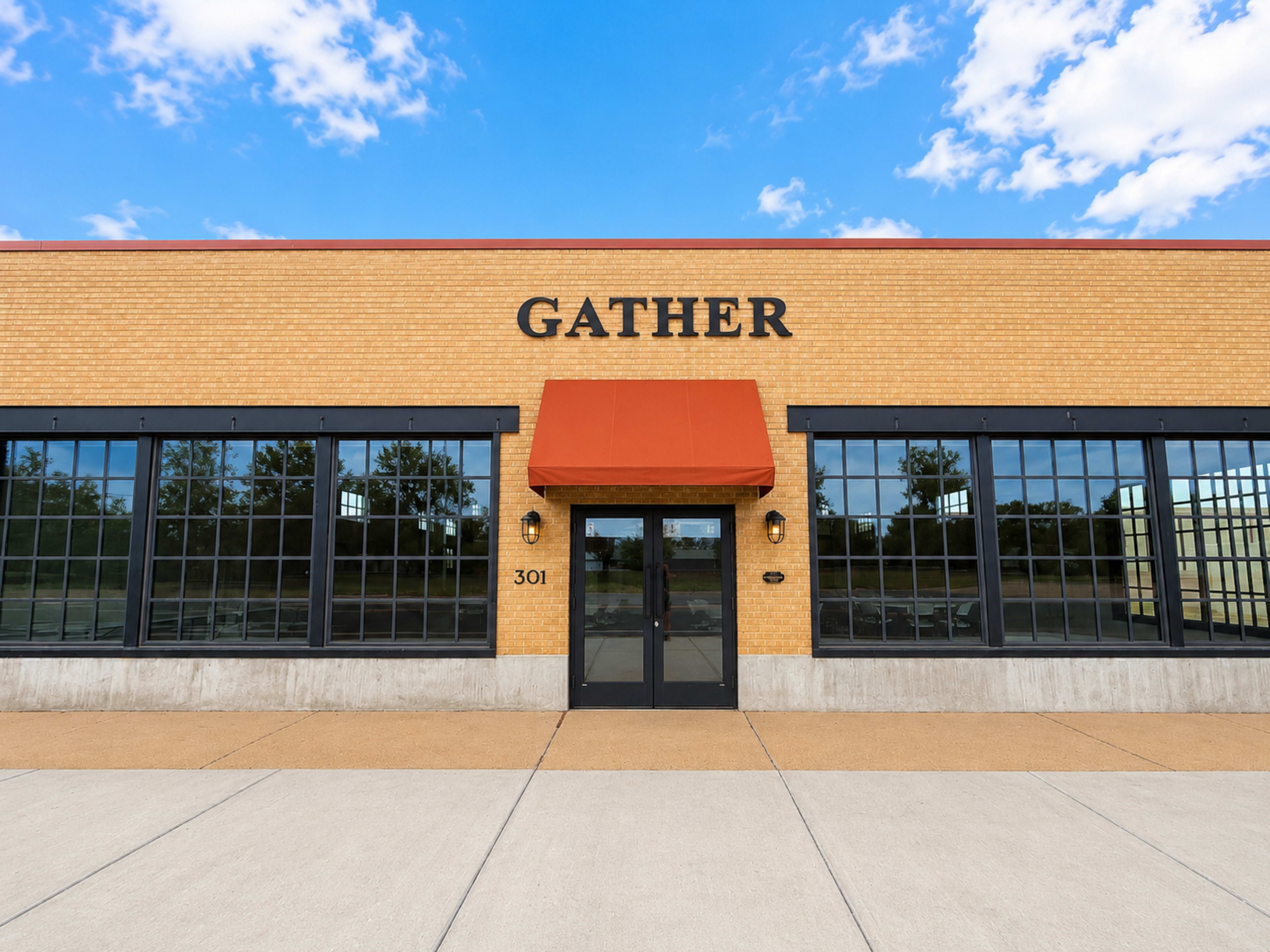 The image shows a brick building with large windows and an orange awning, featuring the word "GATHER" prominently displayed above the entrance.