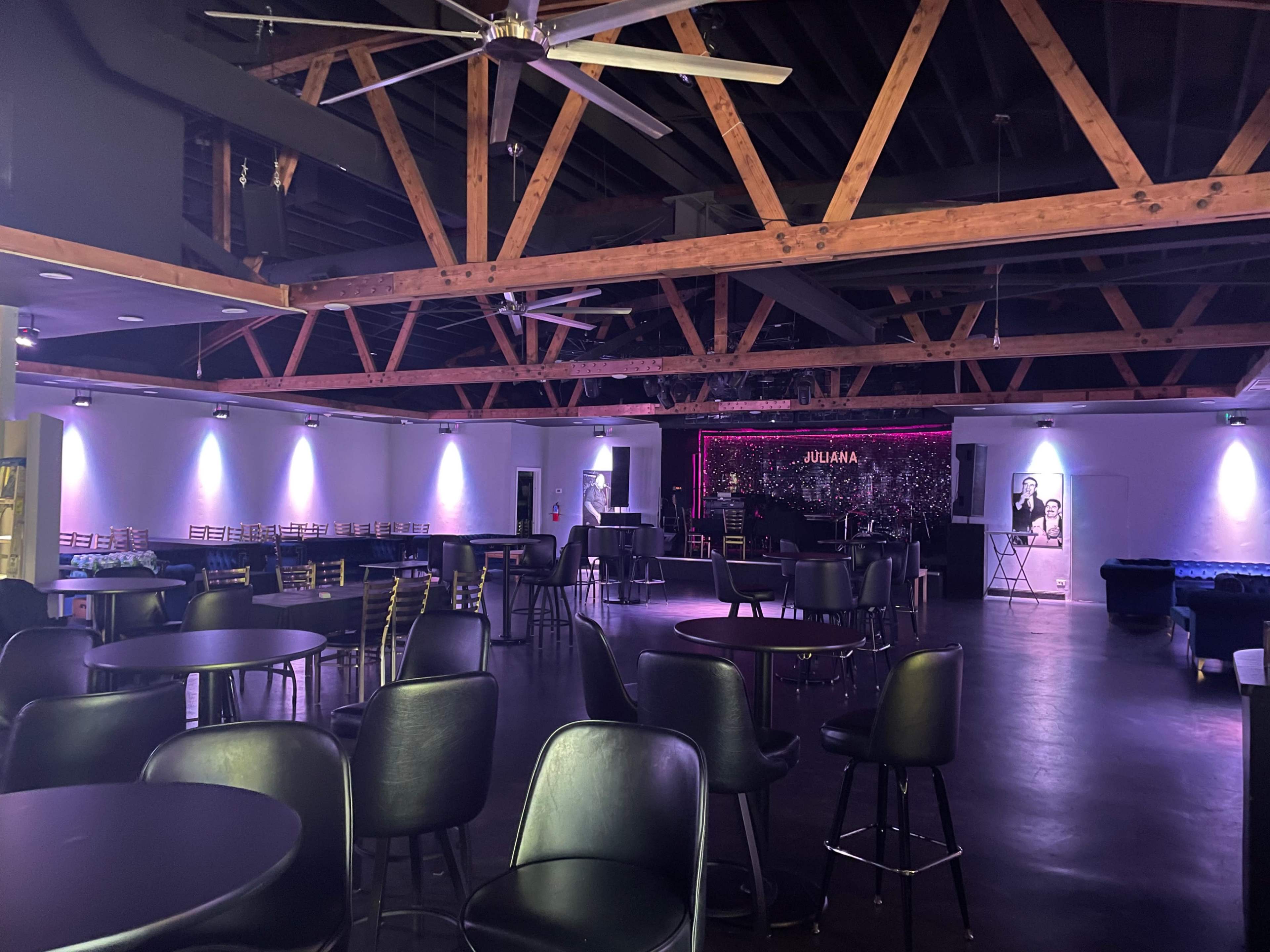 A spacious, dimly lit interior of a bar or nightclub featuring wooden beams and tables arranged in a rectangular layout.