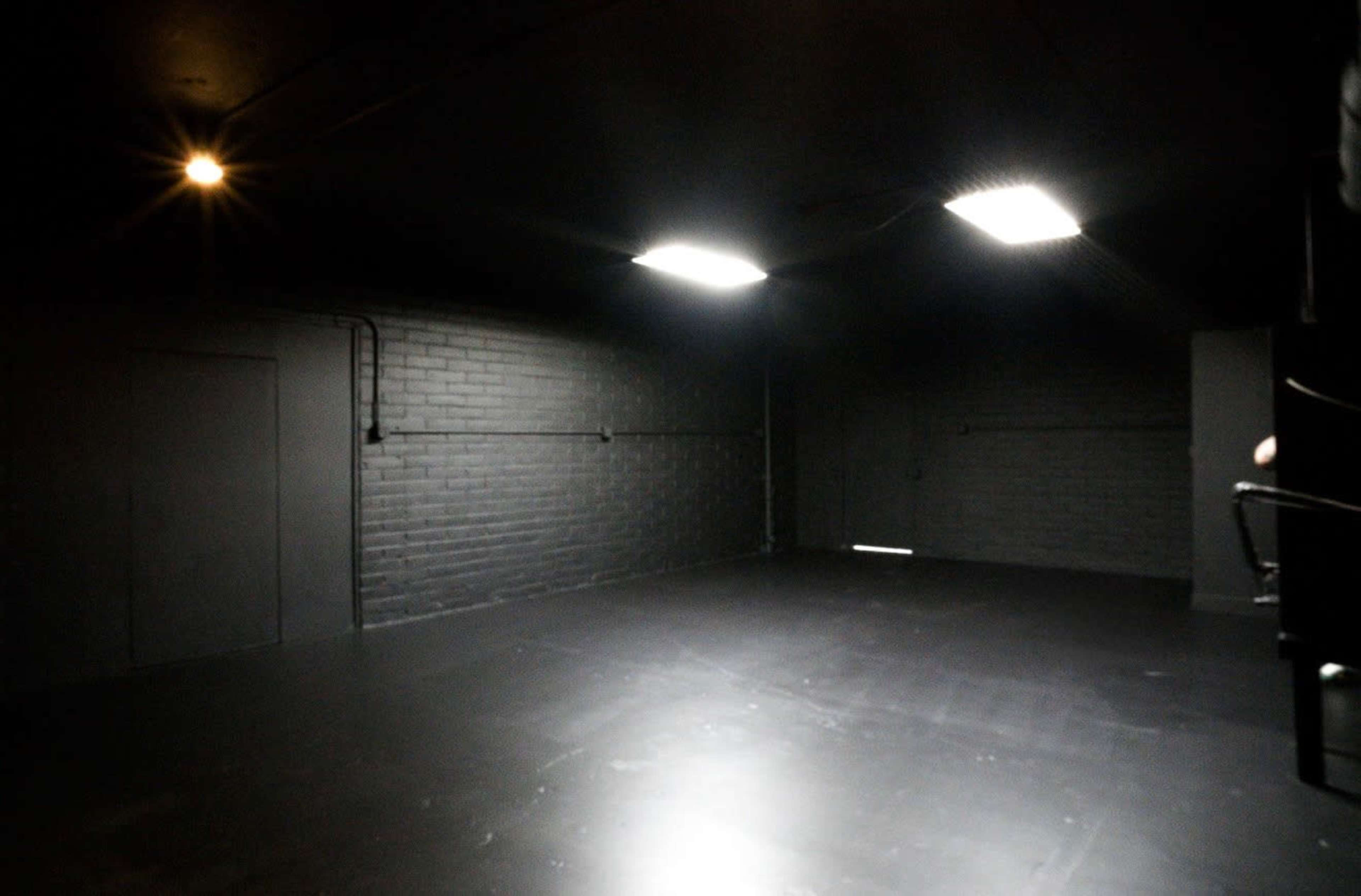 The image shows a dark room with black walls and a smooth floor, illuminated by bright overhead lights.