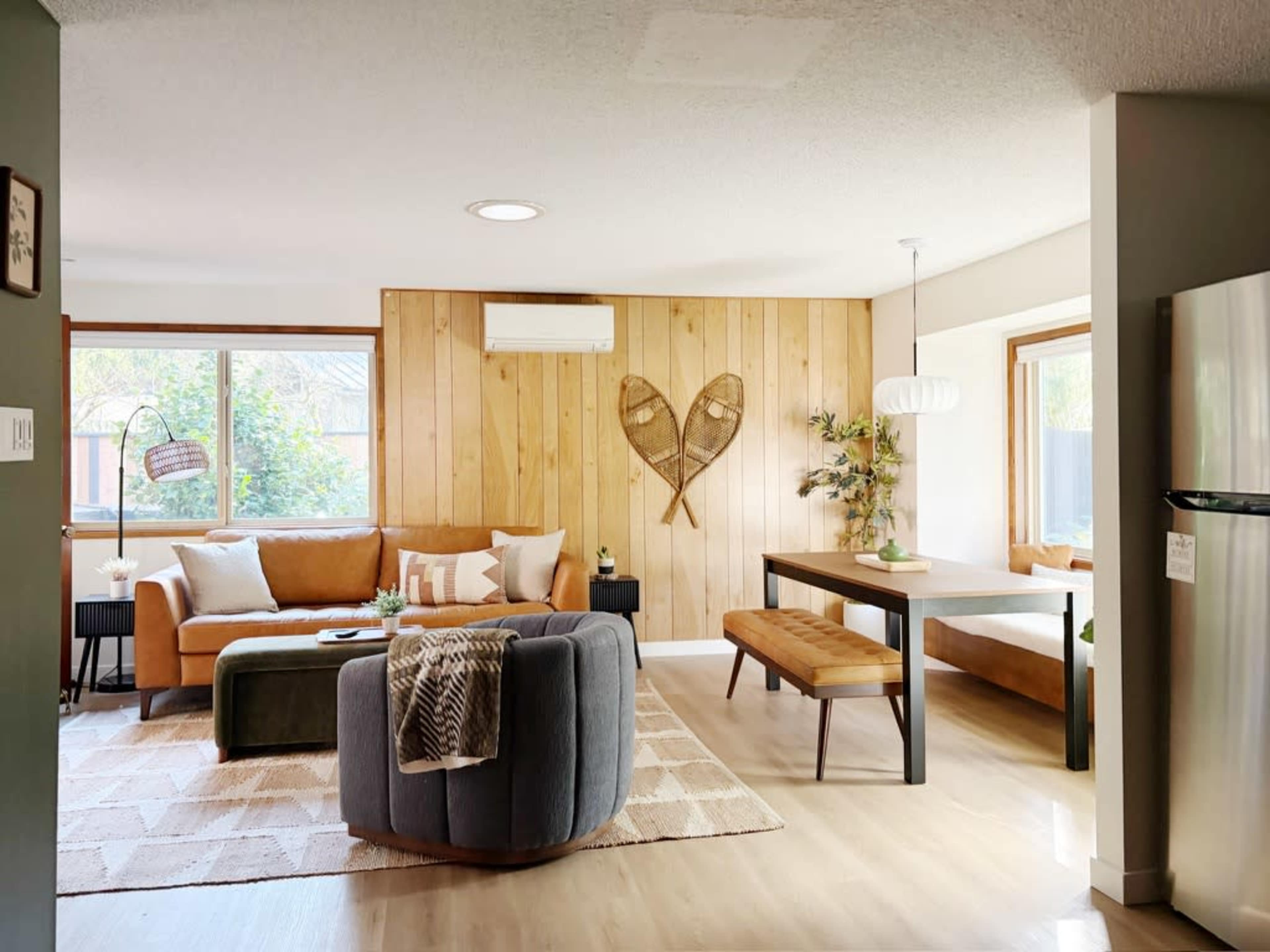 The image shows a modern living space featuring a sofa, a round chair, a wooden dining table, and decorative elements like wall art and plants.