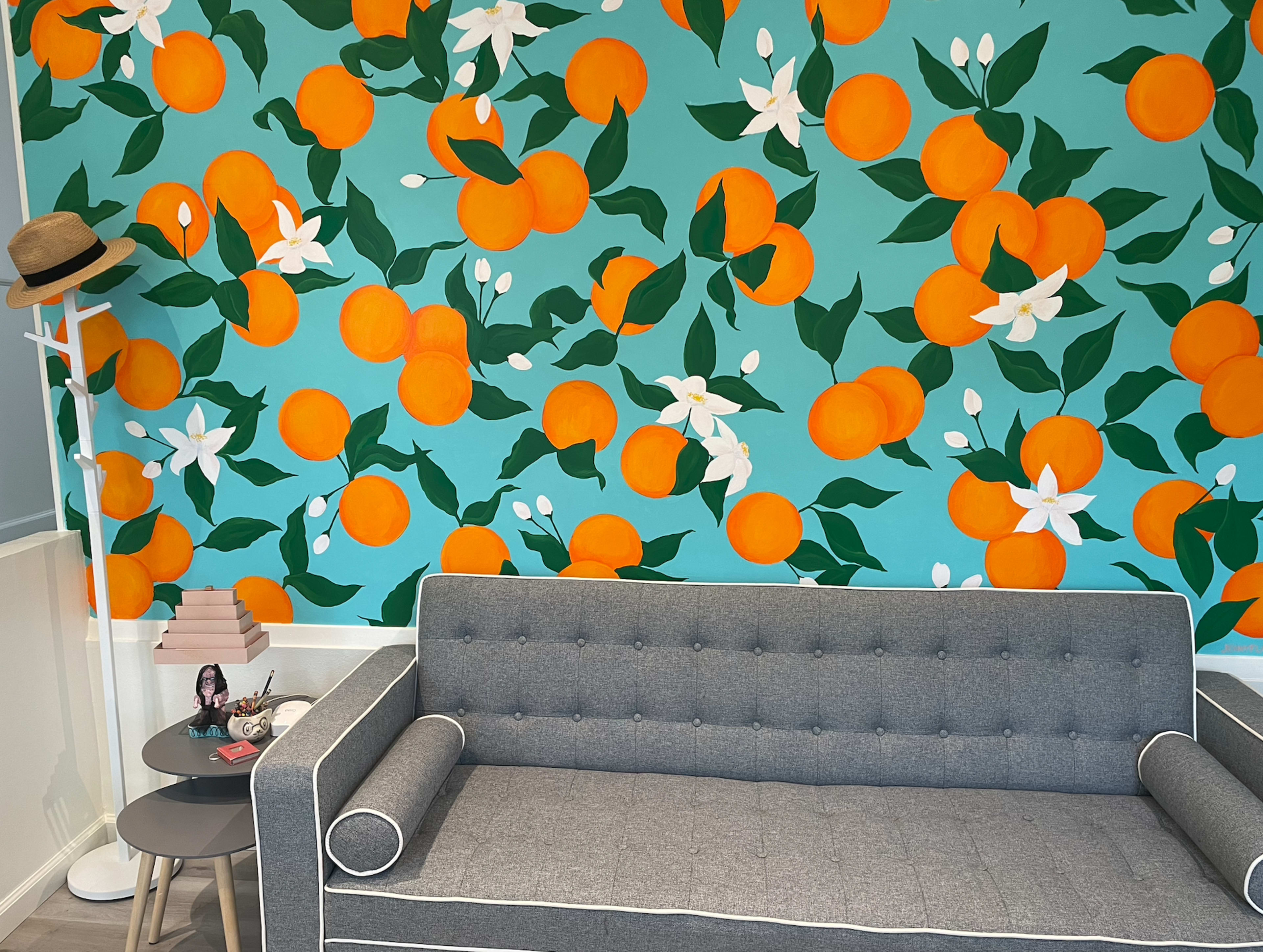 A gray sofa in front of a vibrant mural of oranges and white flowers on a teal wall.