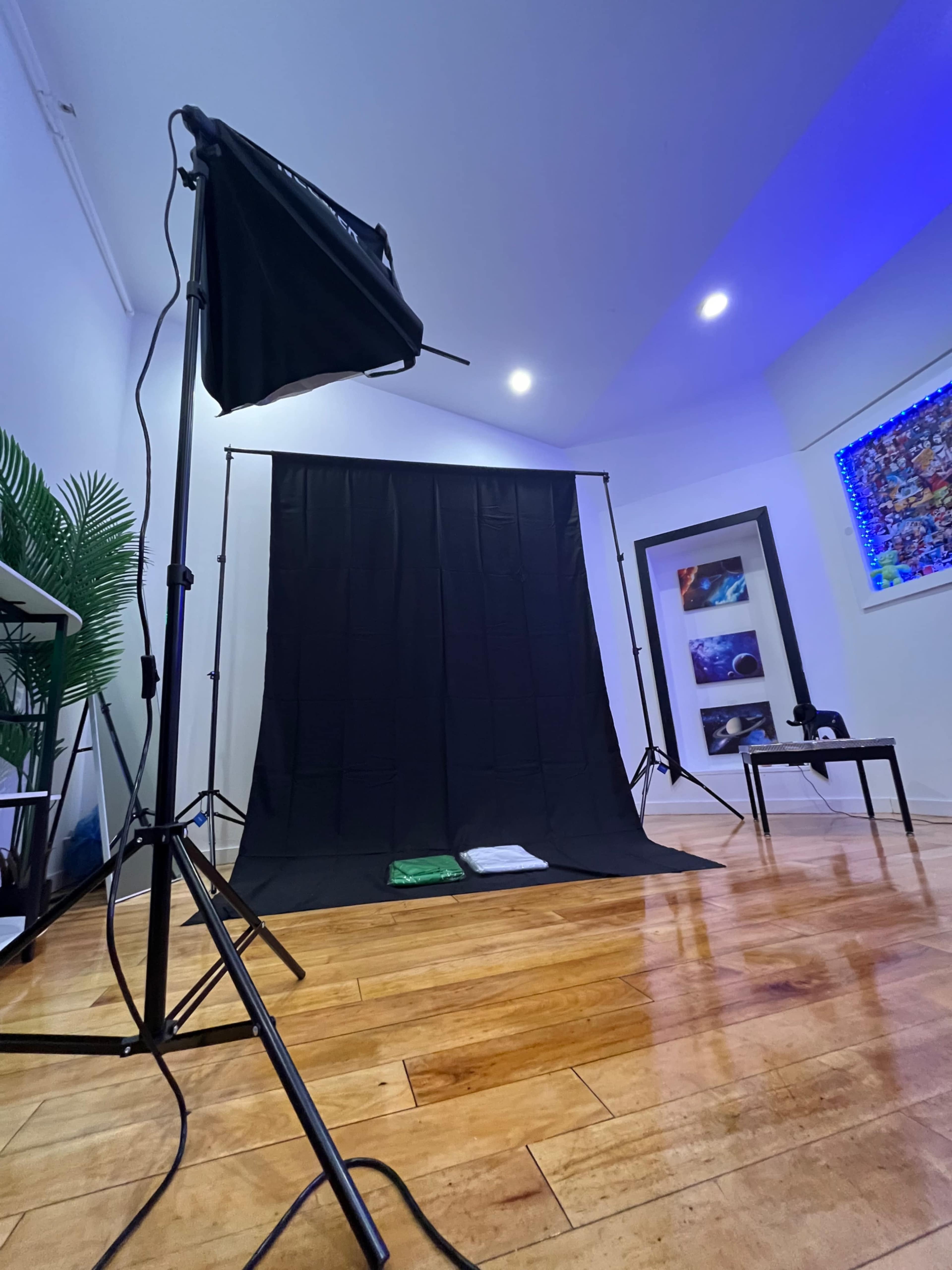 A photography setup with a black backdrop, two light stands, a small table, and a shelf with decorative items in a well-lit room.