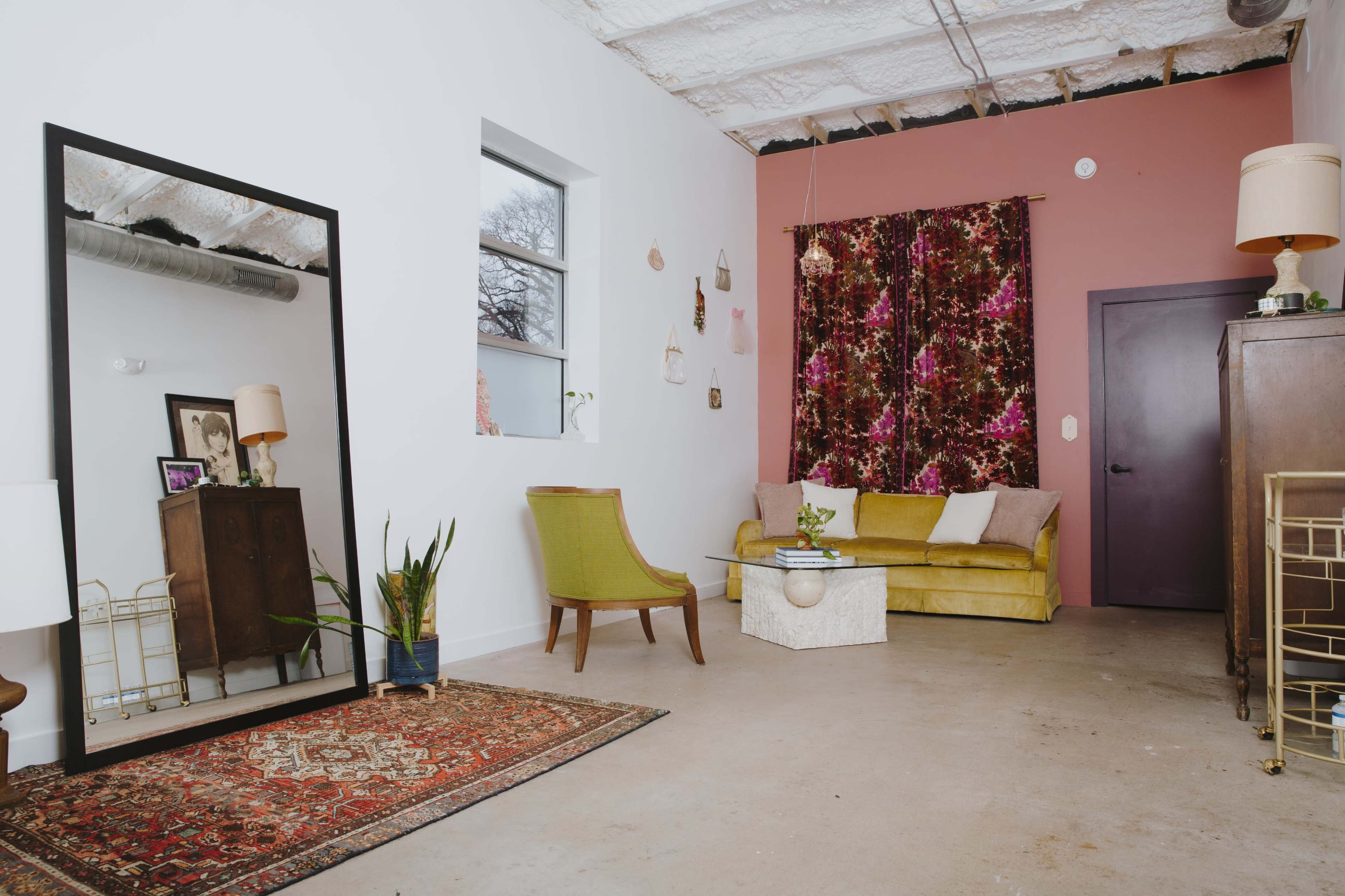 A modern living room featuring a yellow sofa, a mirror, a decorative rug, and a dark wooden cabinet against a painted wall.