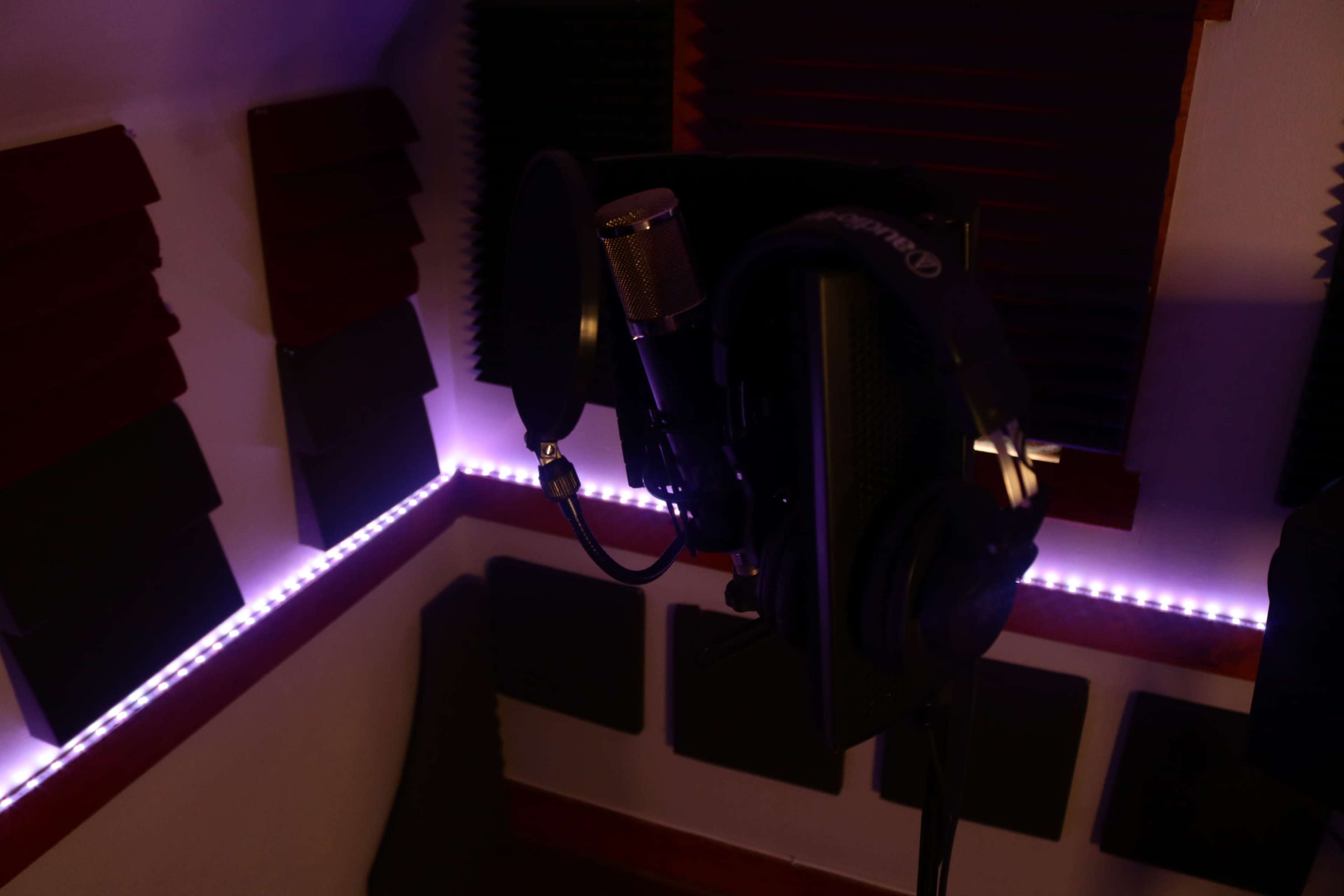 A recording studio booth with a microphone and headphones set up against soundproofed walls.