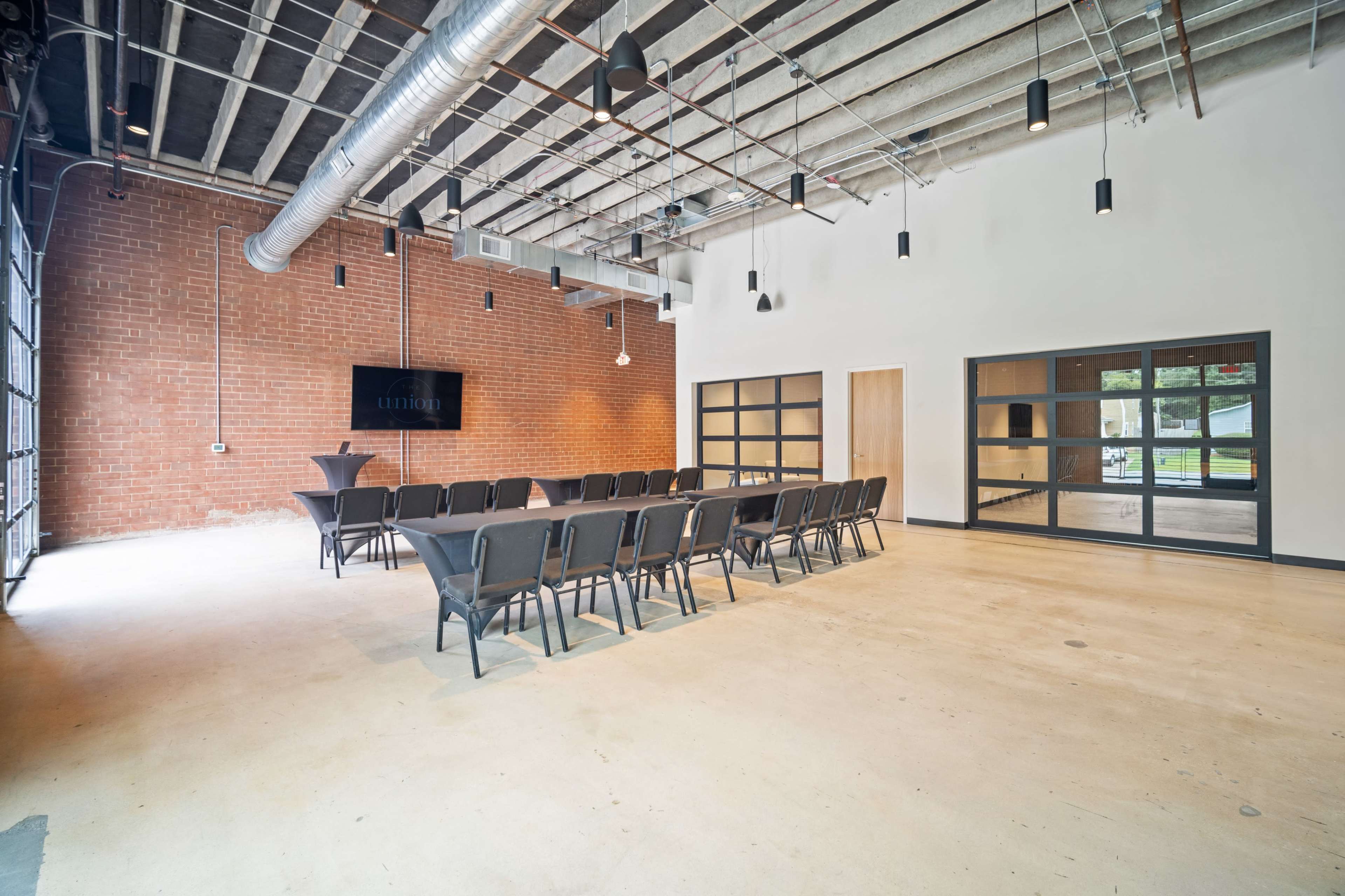 The image shows a spacious conference room with a long table set for a meeting, exposed brick walls, and large windows.