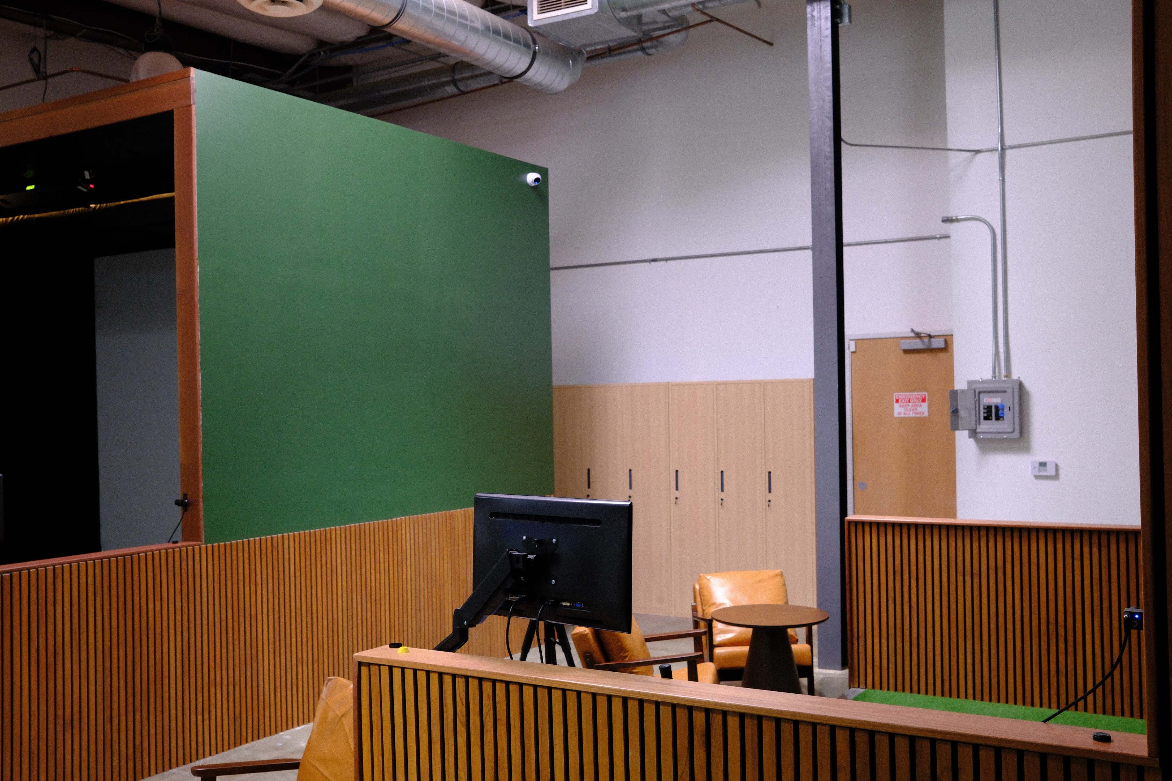 The image shows a modern office space with a green wall, a computer monitor on a stand, and wooden paneling.