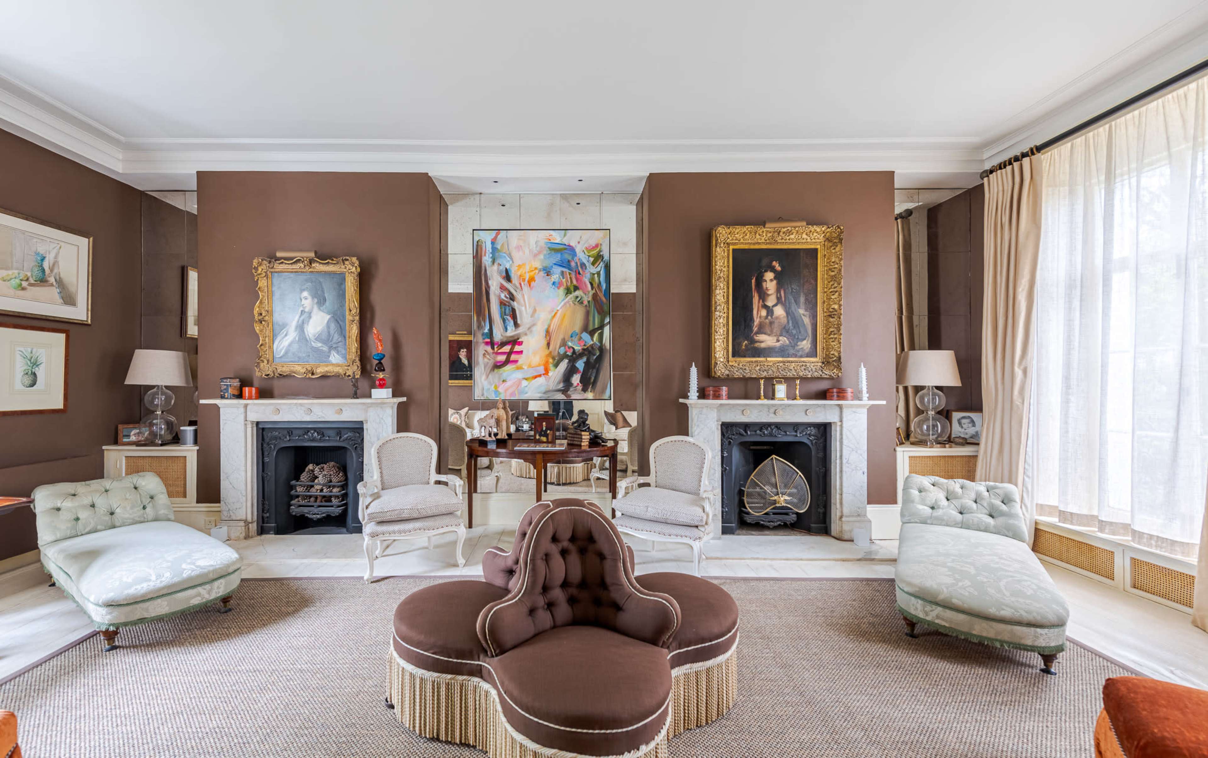 The living room features a symmetrical arrangement of vintage chairs, two ornate paintings on the walls, and a central upholstered sofa on a woven rug.
