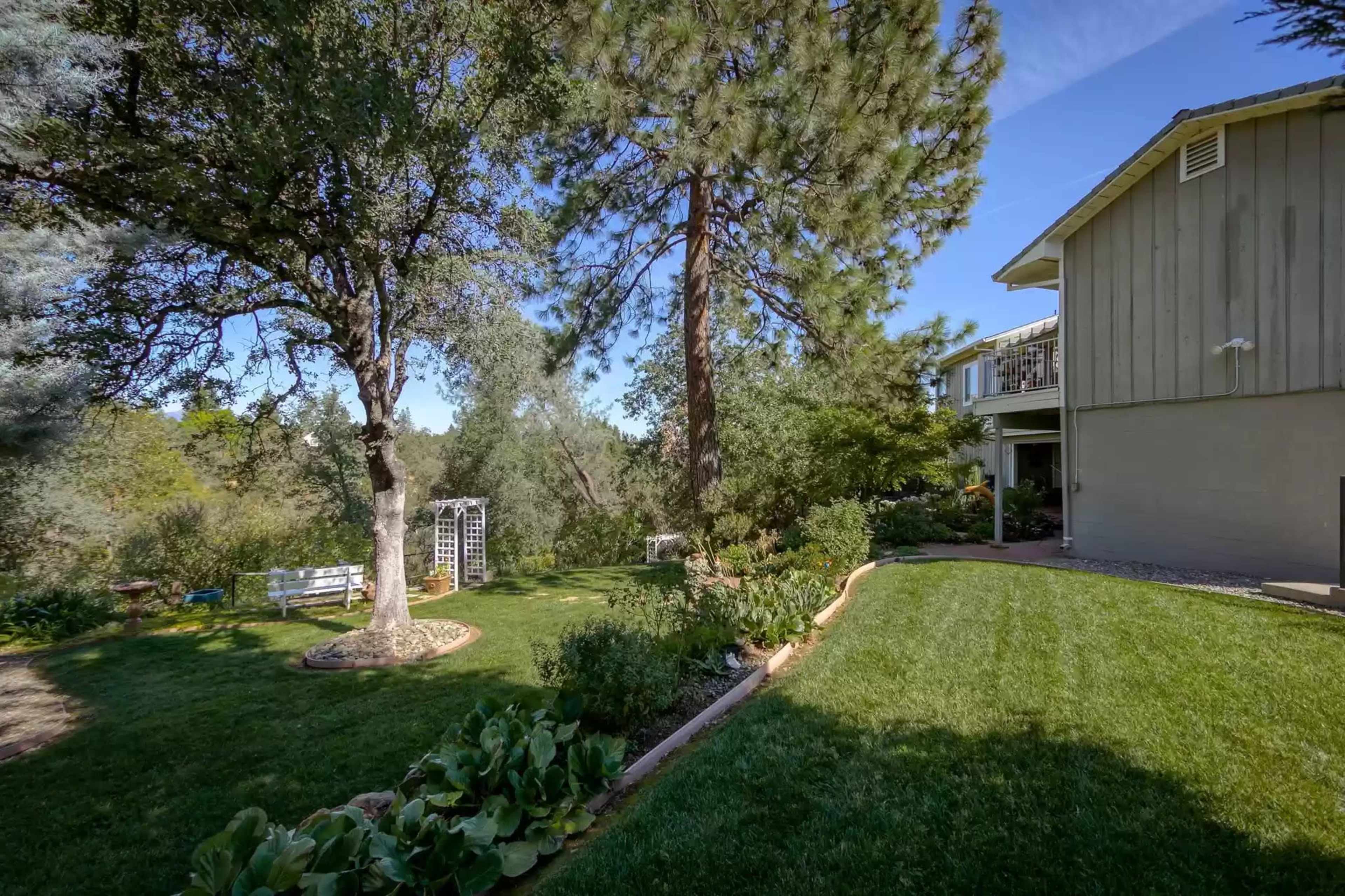 A well-maintained backyard featuring a grassy area, a tree, a garden path, and a house in the background.