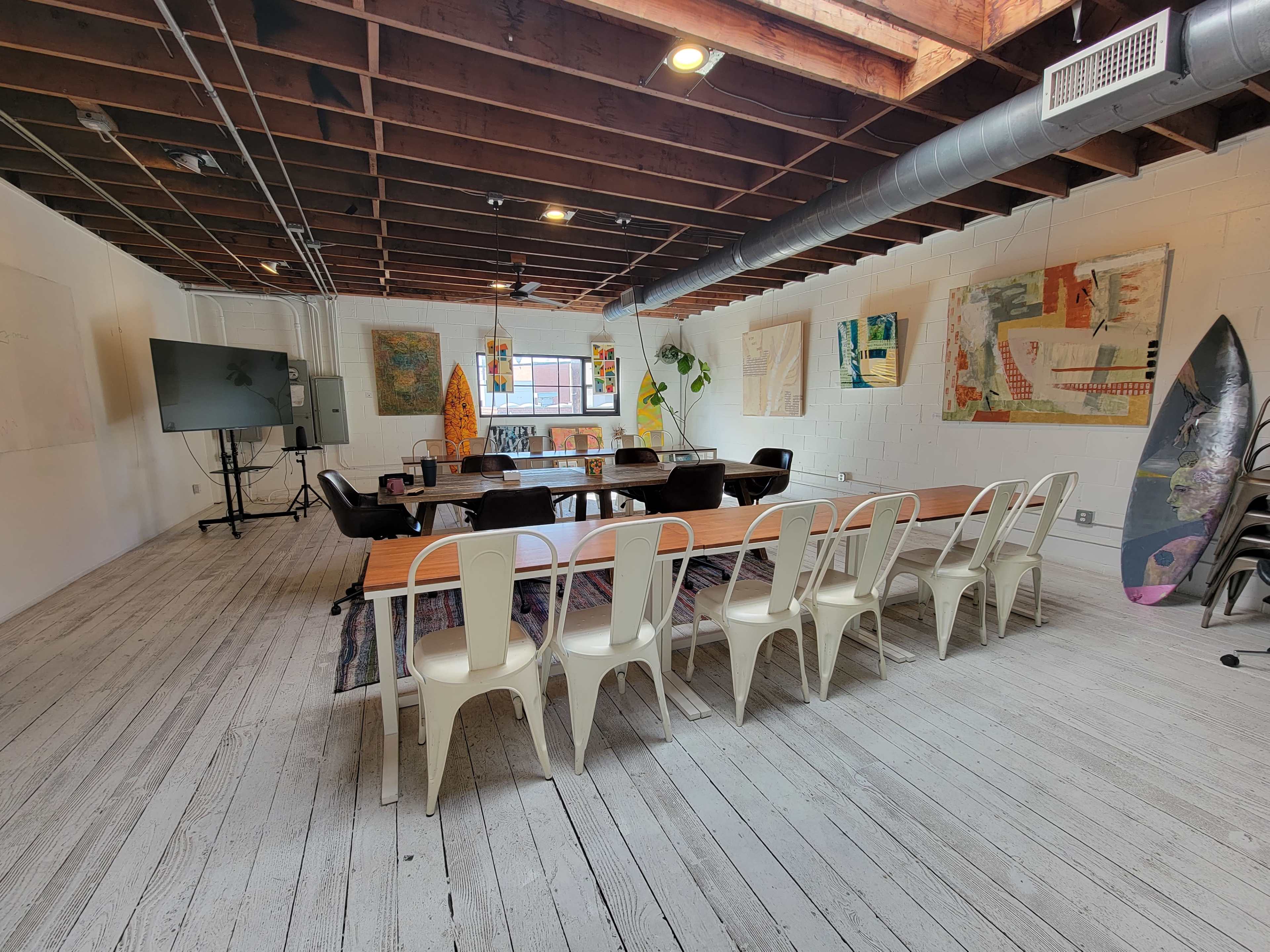 A spacious meeting room features a long wooden table with chairs, a large screen, and artwork displayed on the walls.