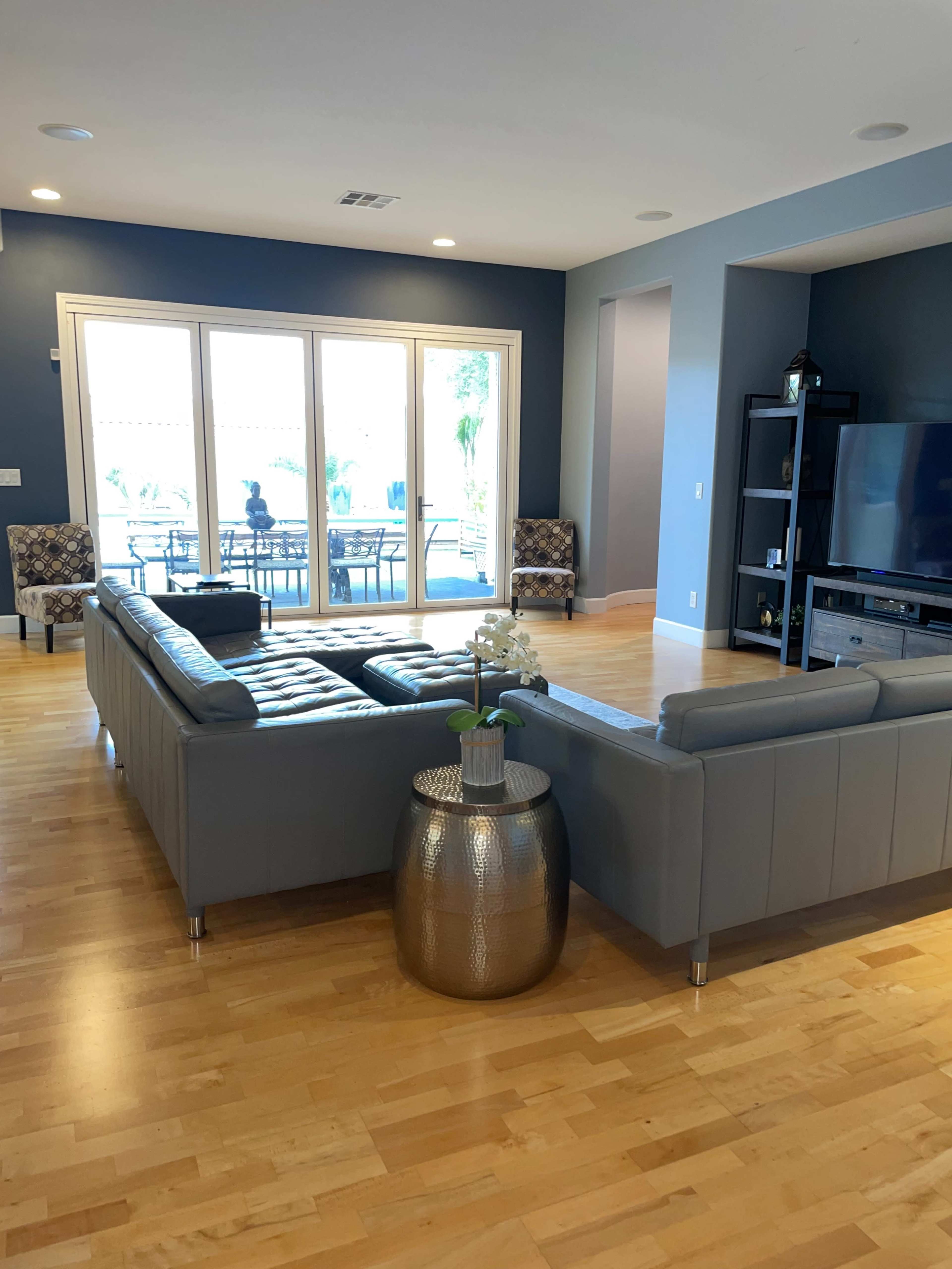 A modern living room with a gray sectional sofa, a circular metallic side table, and large windows leading to a patio area.