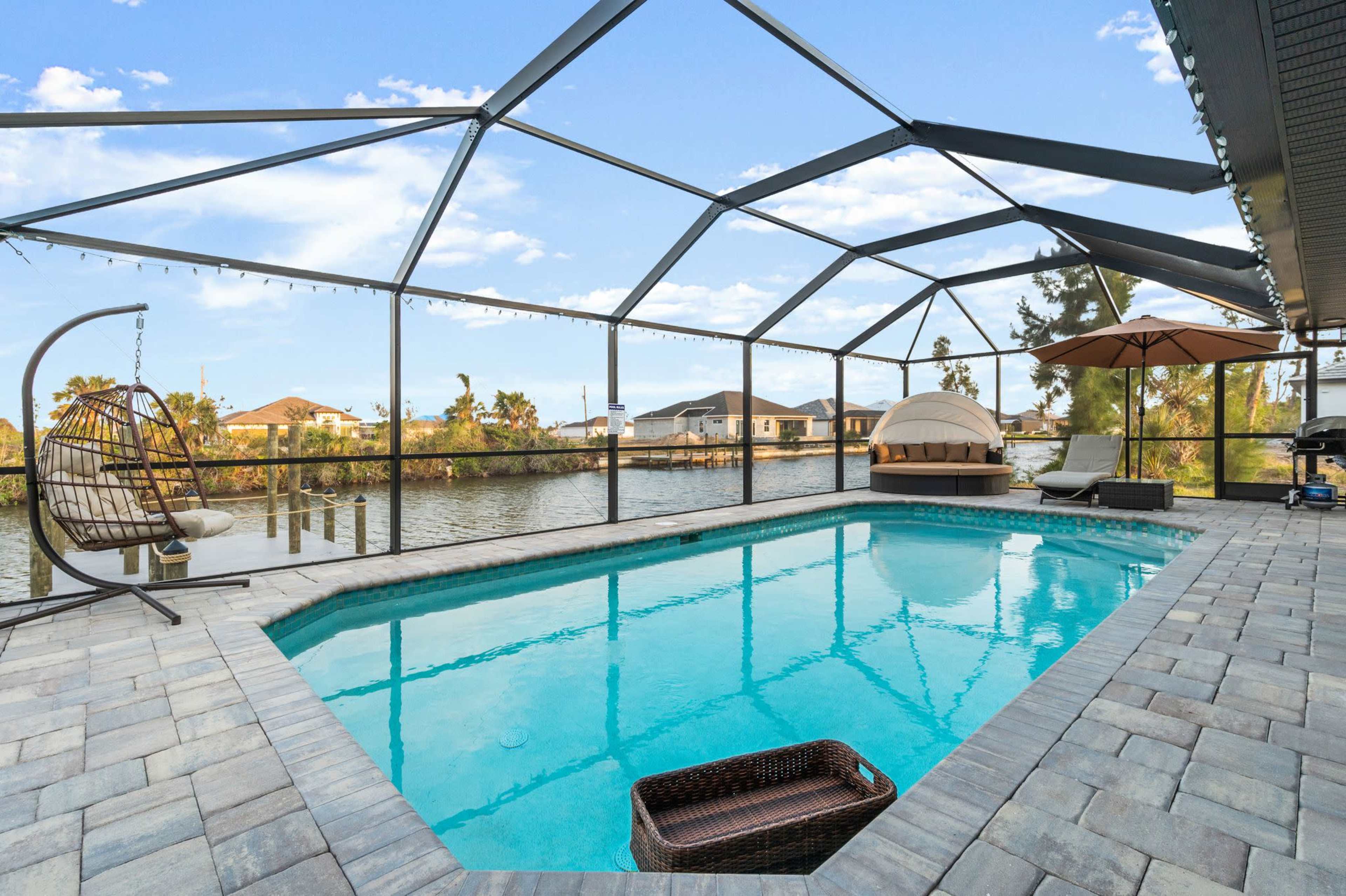 A screened-in swimming pool area with a view of a waterfront and several homes in the background.