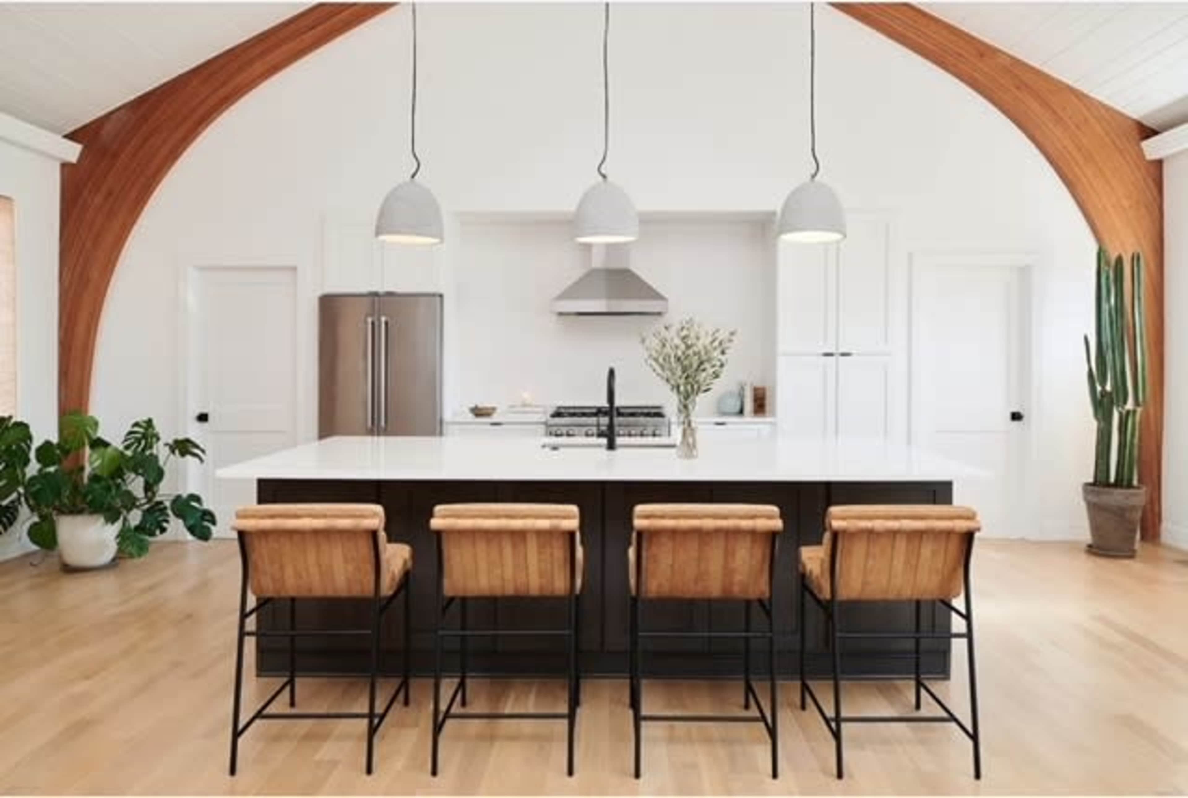 A modern kitchen features a central island with bar stools, stainless steel appliances, and a large cactus in a pot.