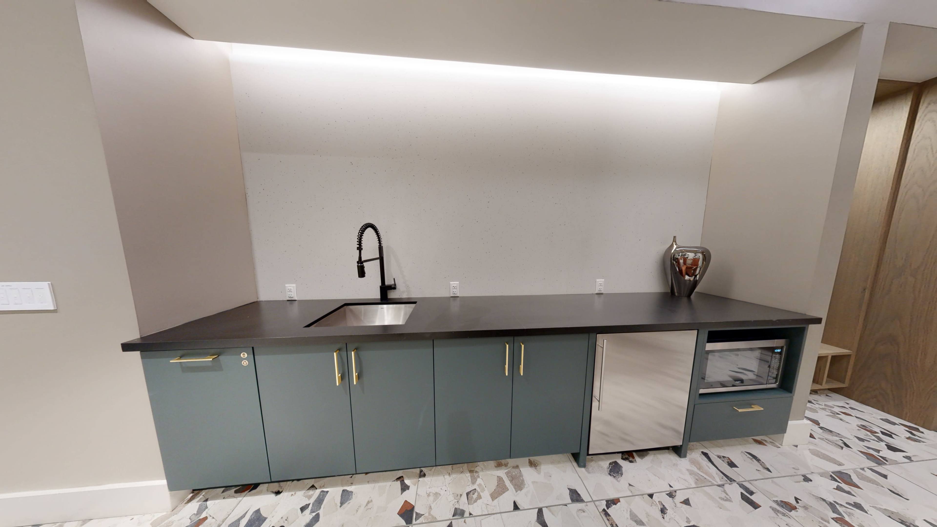 A modern kitchen countertop with a sink, a microwave, and storage cabinets beneath, all set against a light-colored wall with a backlight.