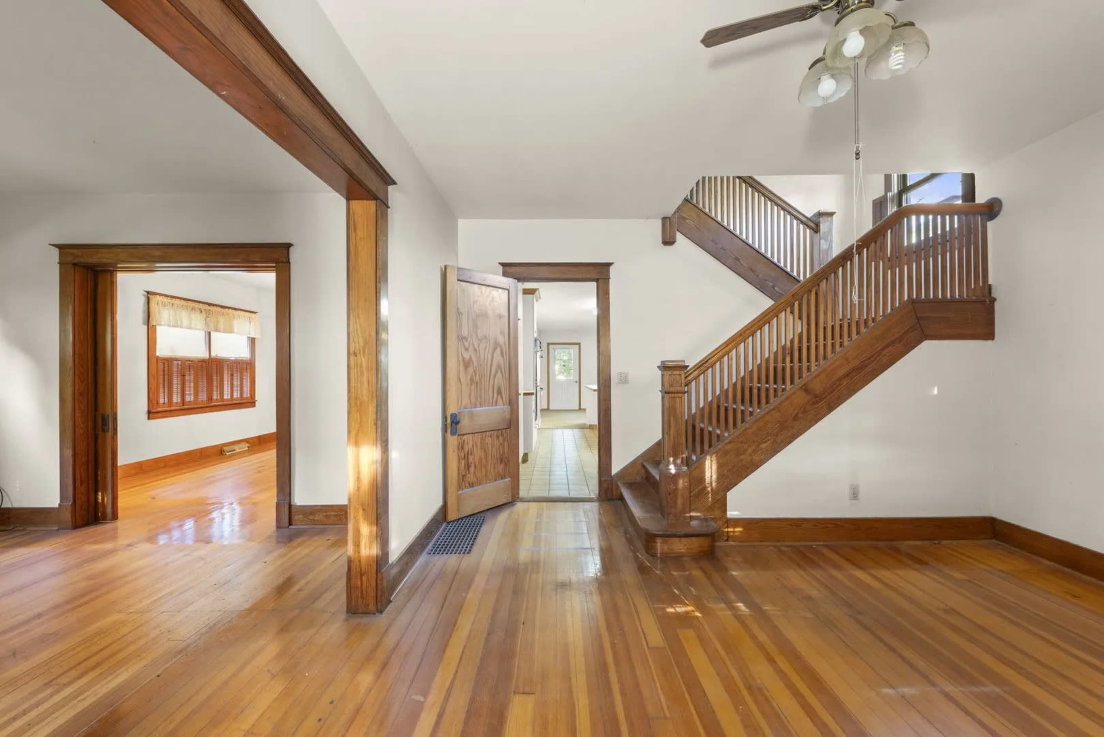 The image shows a spacious interior with wooden floors, an open doorway, and a staircase leading to the second level.