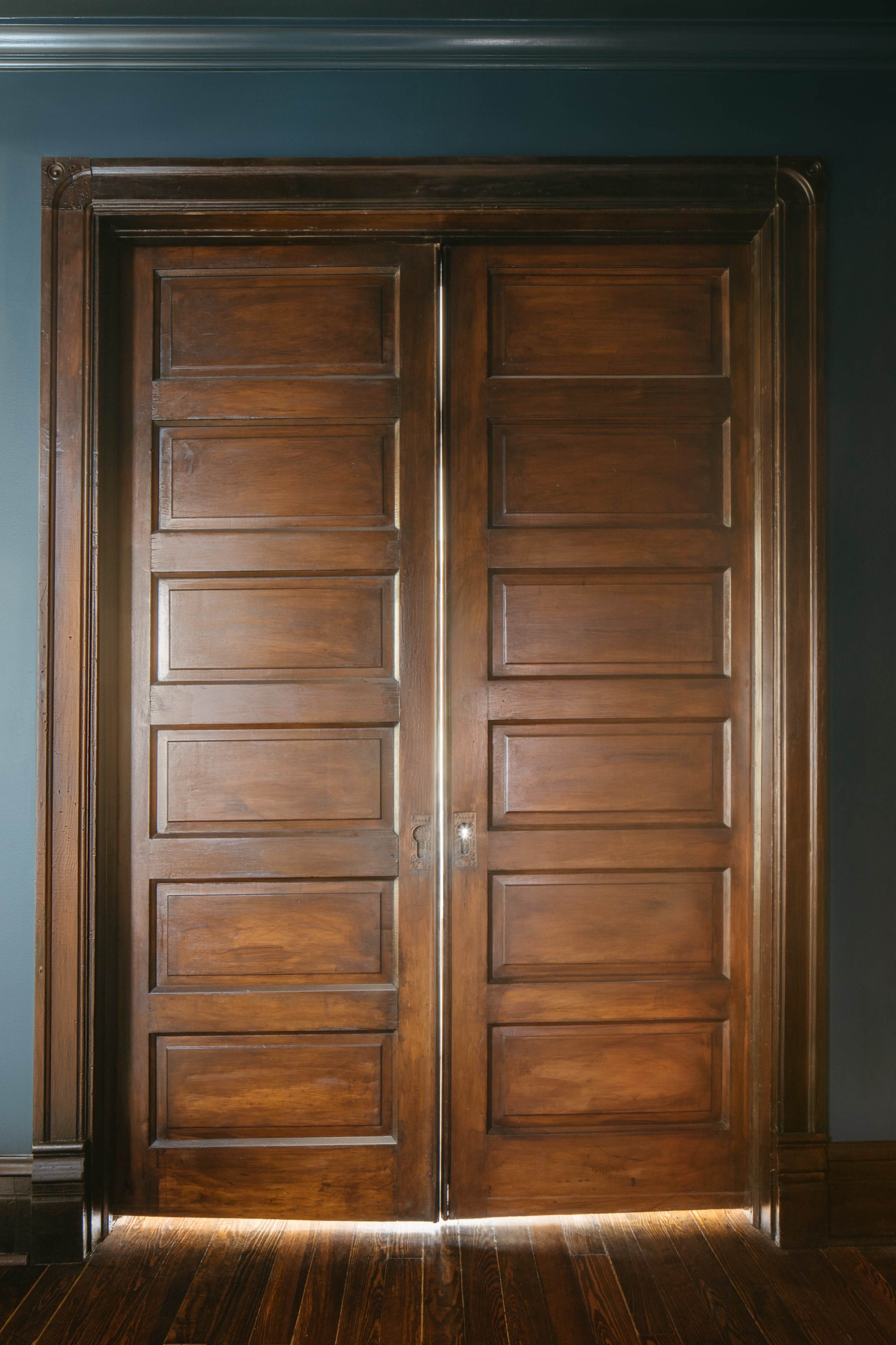 A pair of wooden double doors with a polished finish stands closed against a dark-colored wall.