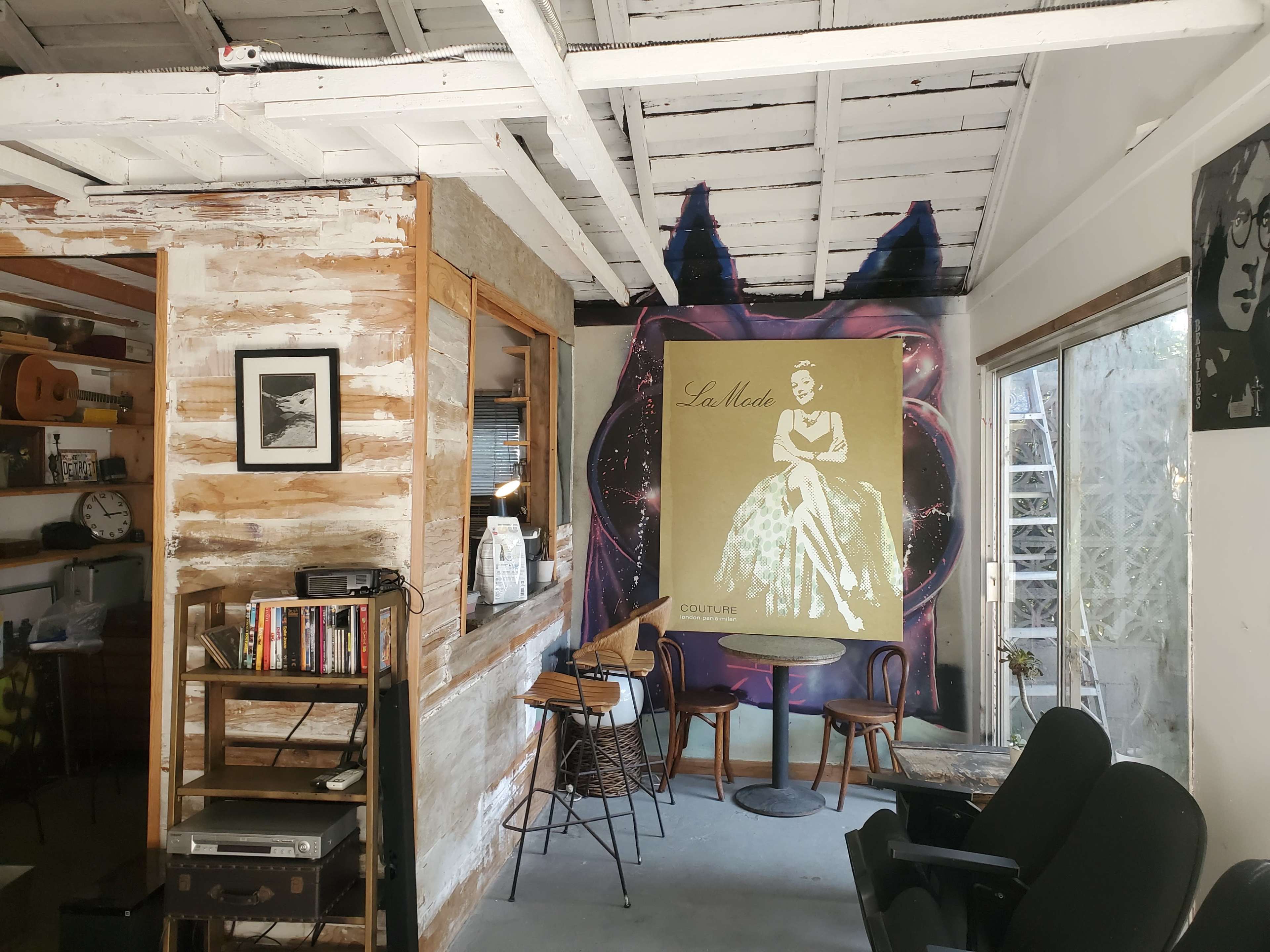 The scene features a rustic interior with a wooden counter, bookshelves, and a large fashion poster against the wall.