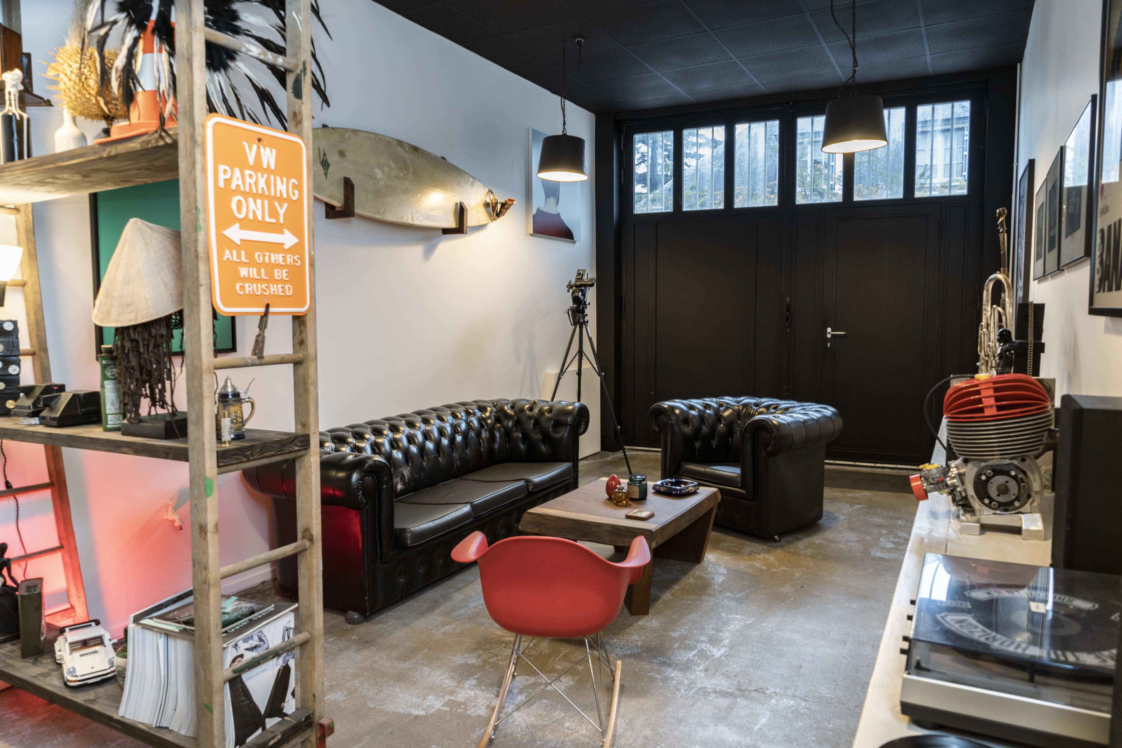 A modern lounge area with black leather sofas, a wooden shelf displaying various decor items, and a vinyl record player on a side table.