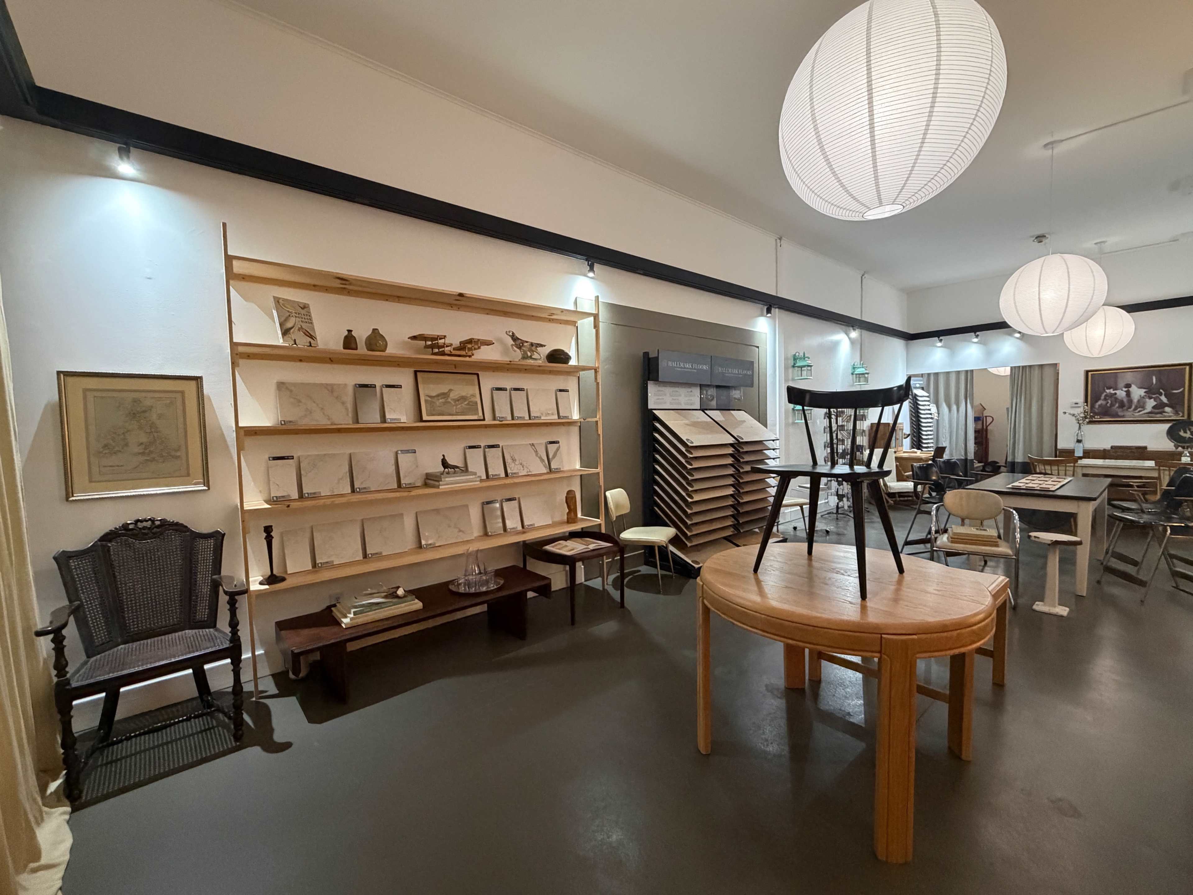 The image shows an interior space featuring wooden shelves filled with framed documents, a round table, a chair on a pedestal, and various furniture pieces under soft lighting.