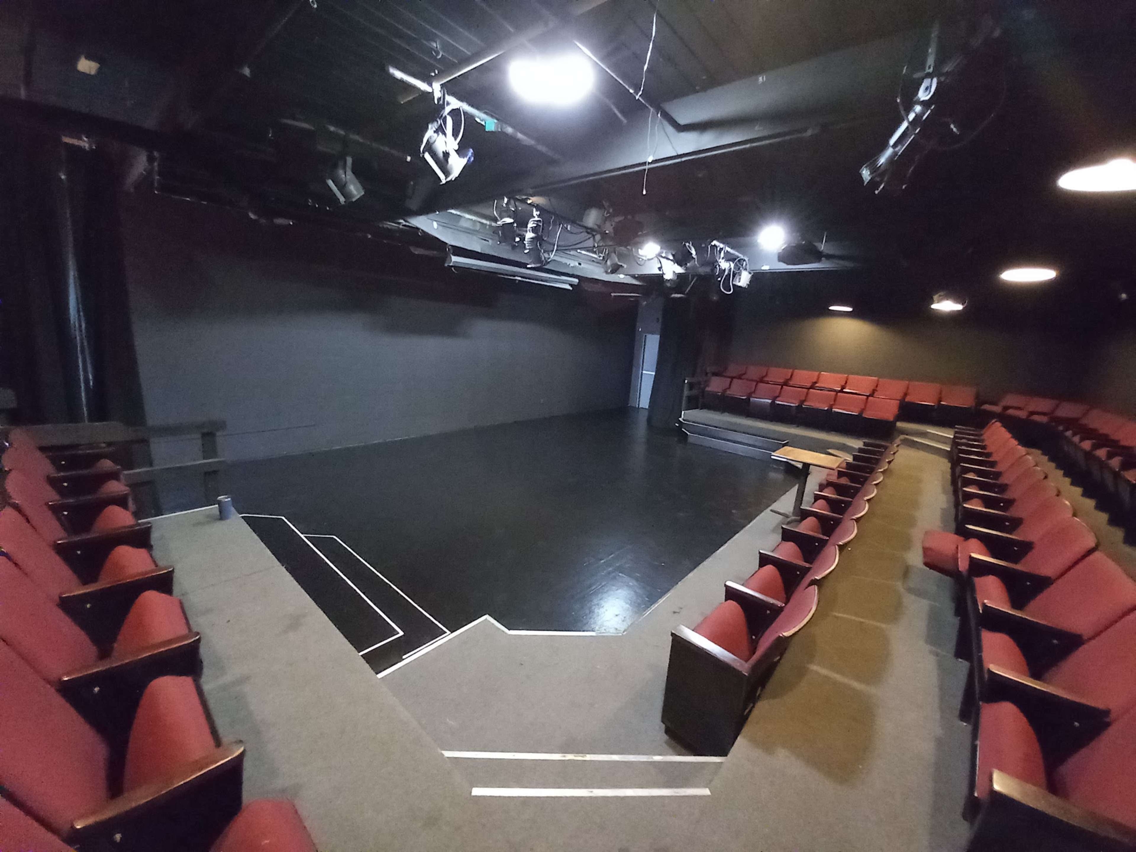 A small theater with red seating arranged in a semi-circular layout facing a polished black stage.